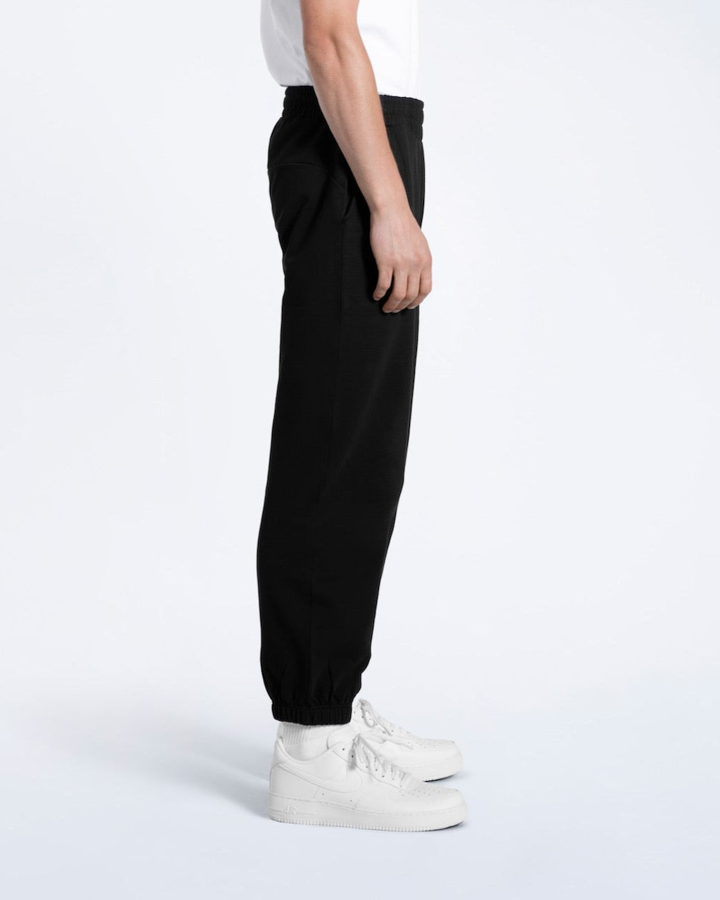 A person facing side on, modelling a pair of men's black heavyweight organic cotton joggers.