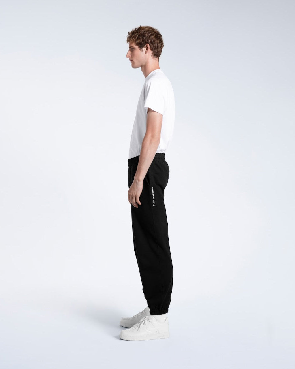 A man facing side on with his arms by his sides, modelling a pair of black heavyweight organic cotton joggers.