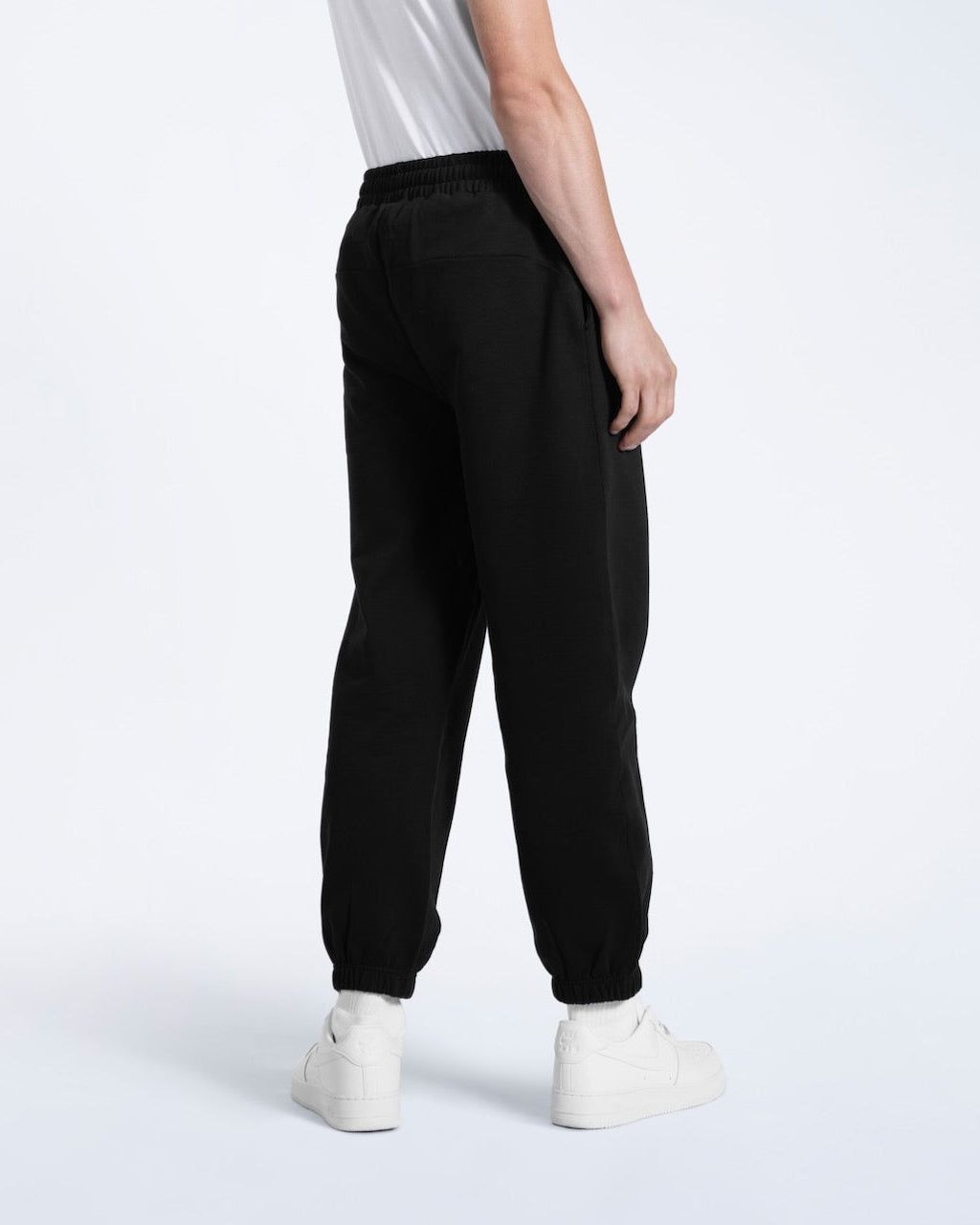 A person facing away from the camera, modelling a pair of men's black heavyweight organic cotton joggers.