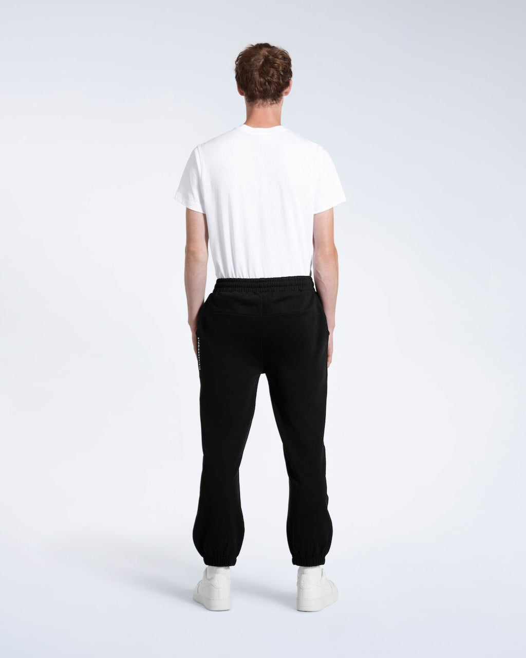A man with his back to the camera with his arms by his sides, modelling a pair of black heavyweight organic cotton joggers.