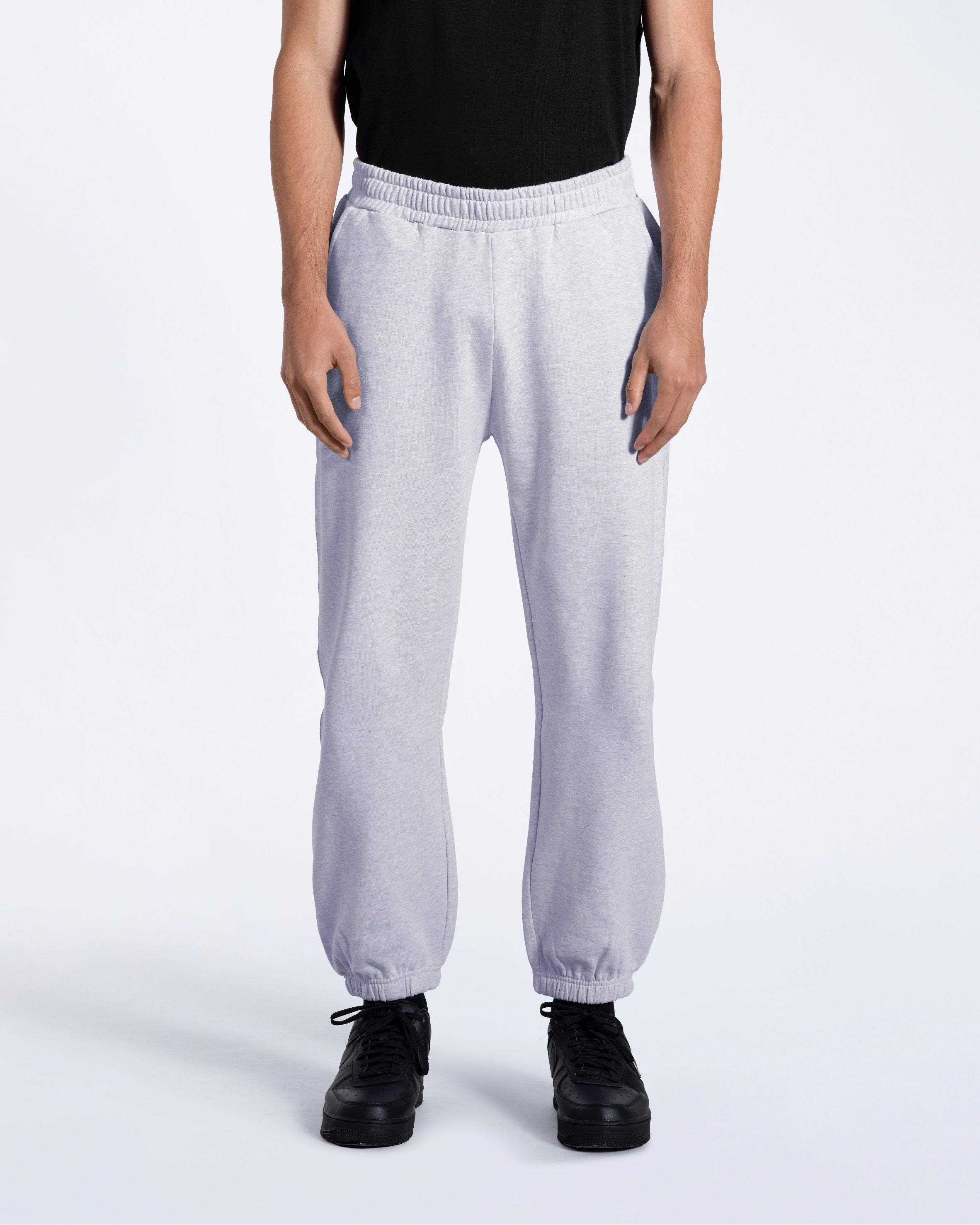 A person with their arms by their sides, modelling a pair of men's grey heavyweight organic cotton joggers.
