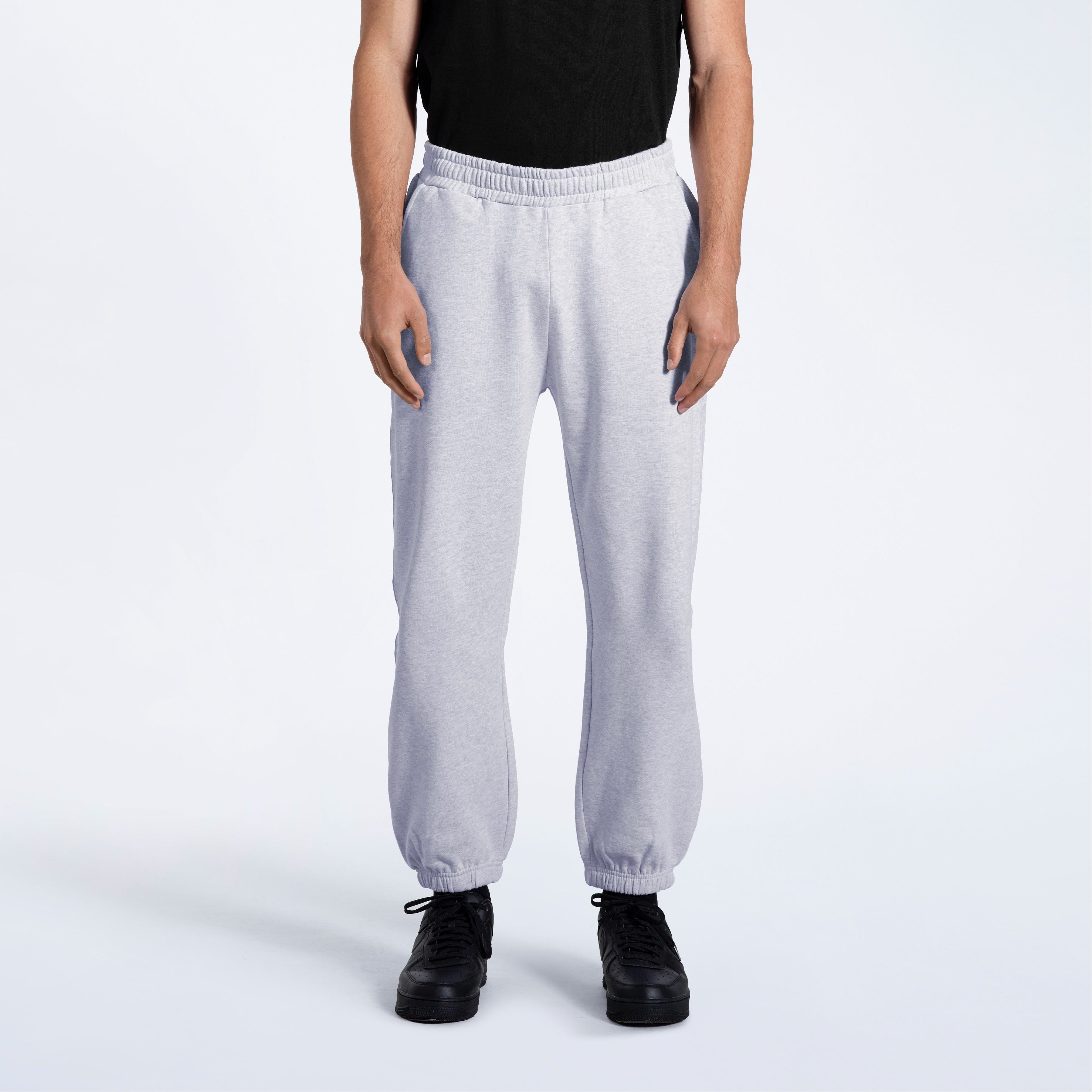 A person with their arms by their sides, modelling a pair of men's grey heavyweight organic cotton joggers.
