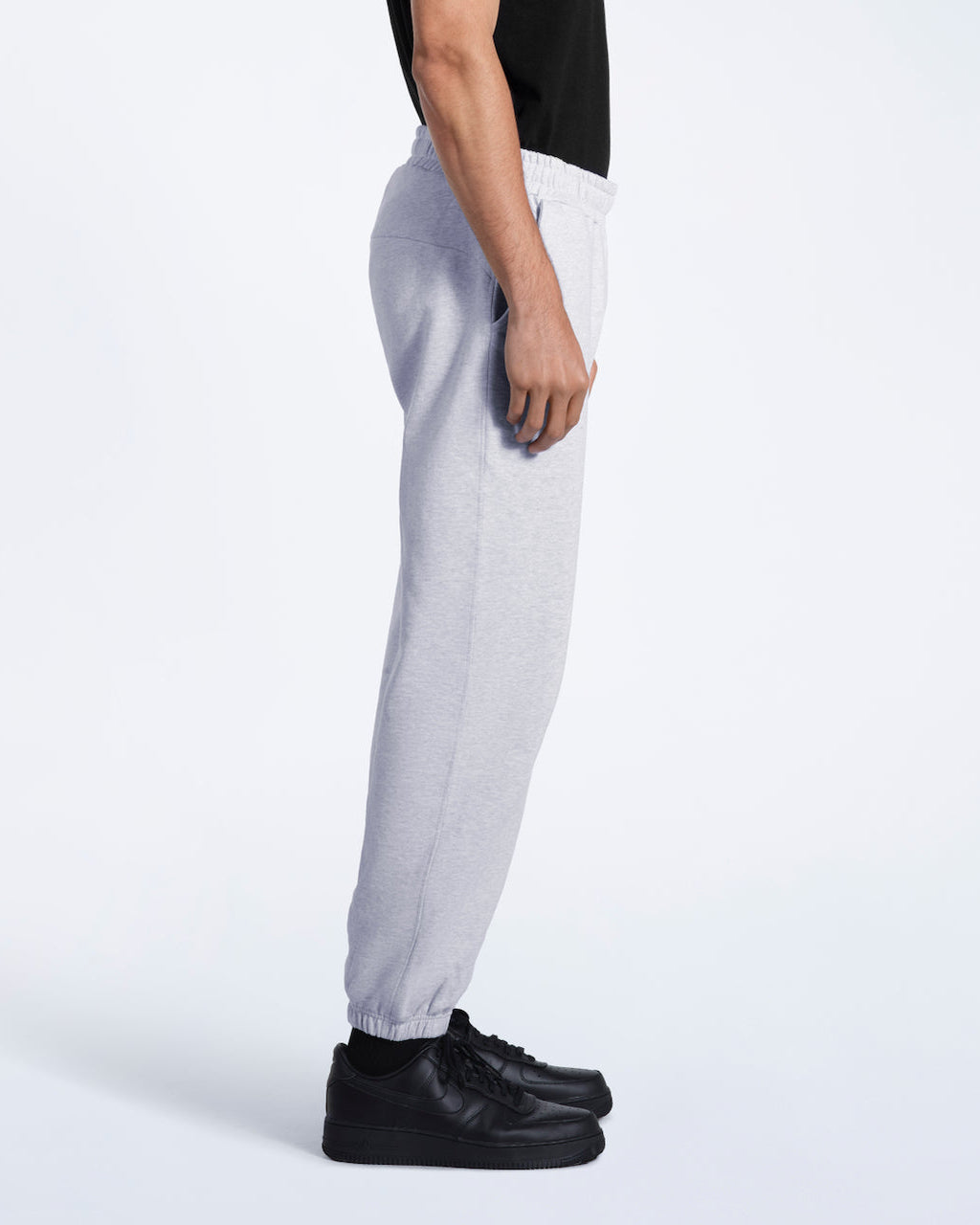 A person facing side on, modelling a pair of men's grey heavyweight organic cotton joggers.