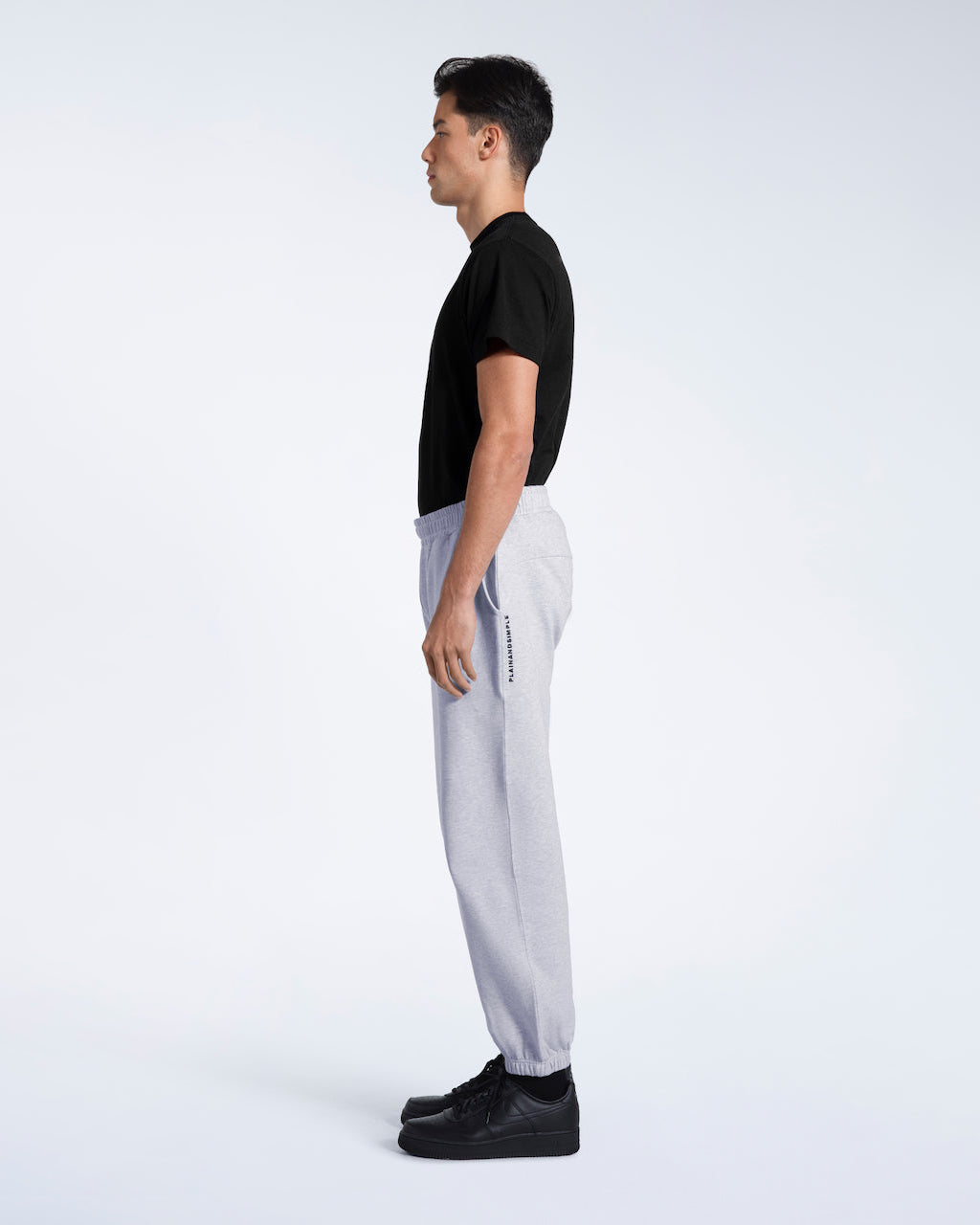 A man facing side on with his arms by his sides, modelling a pair of grey heavyweight organic cotton joggers.