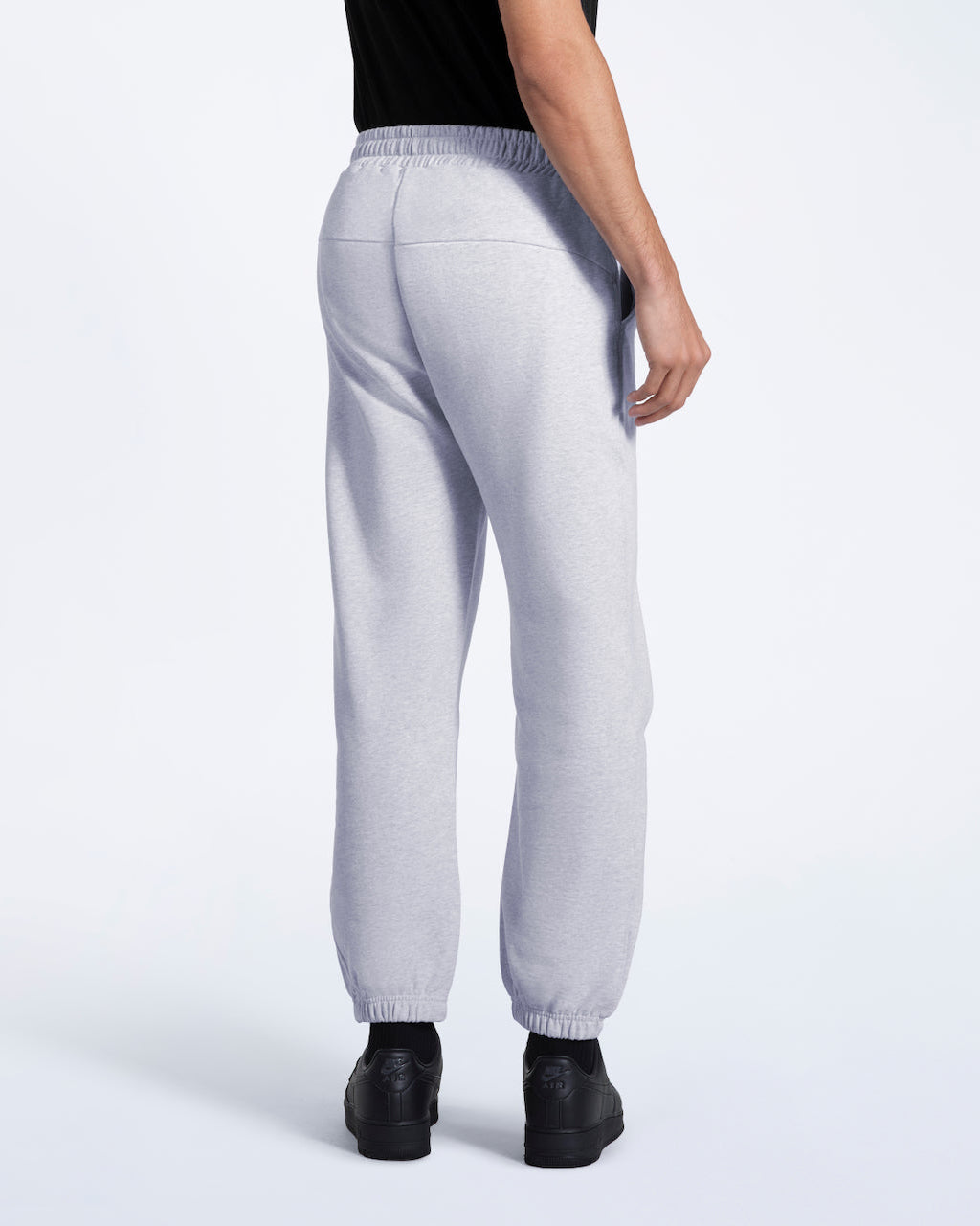 A person facing away from the camera, modelling a pair of men's grey heavyweight organic cotton joggers.