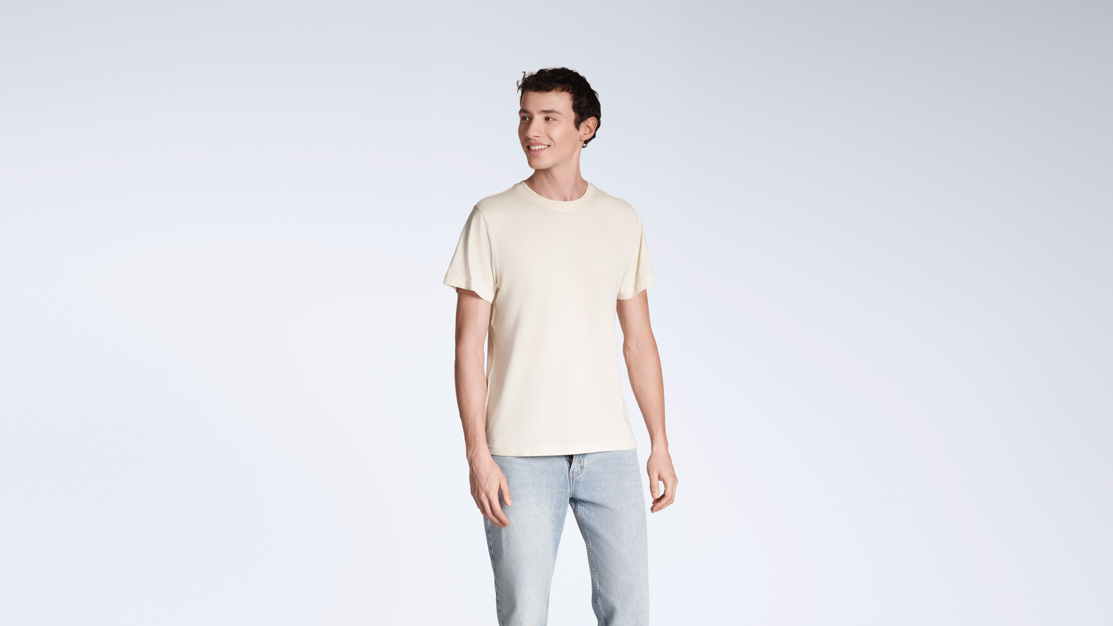 A man smiling, looking away from the camera, modelling a plain, natural coloured, organic cotton t shirt.