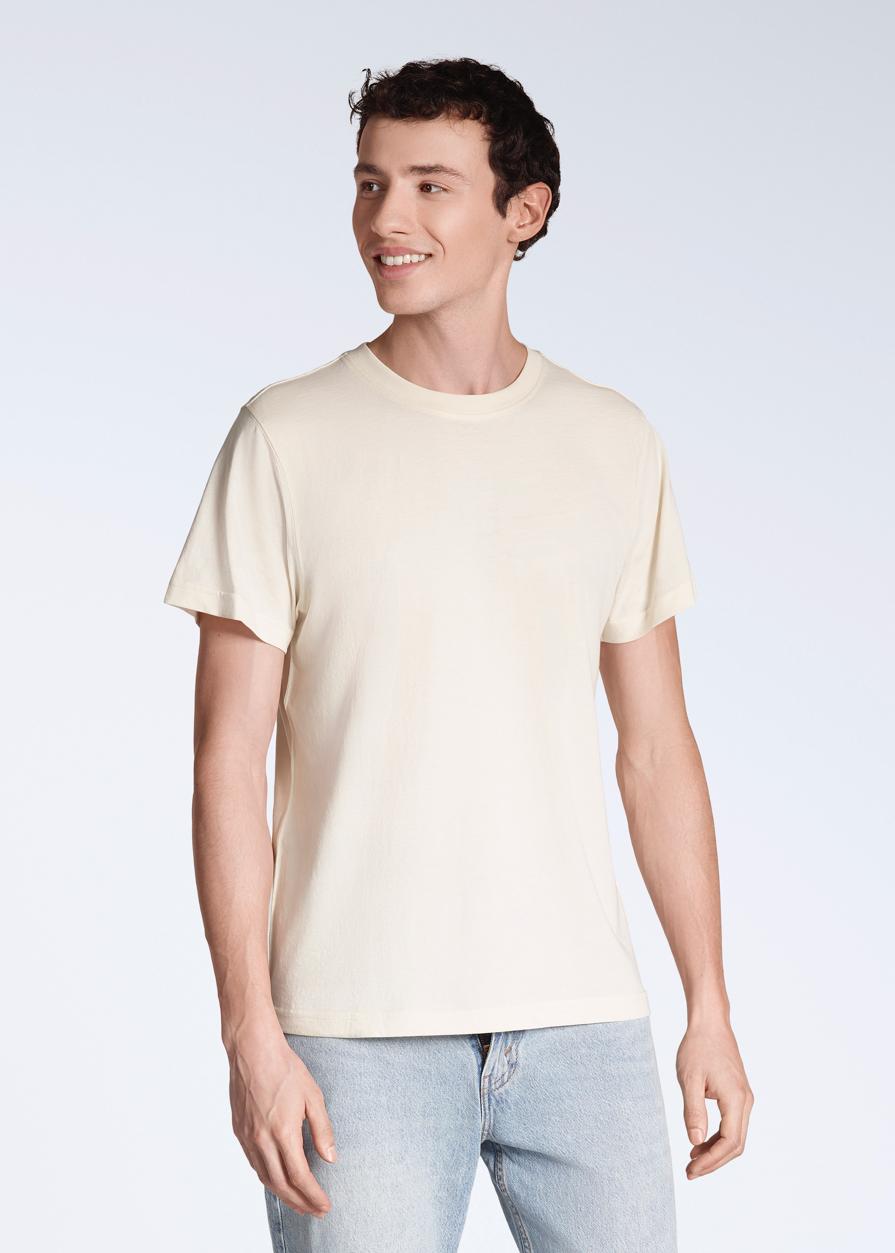 A man smiling, looking away from the camera, modelling a plain, natural coloured, organic cotton t shirt.