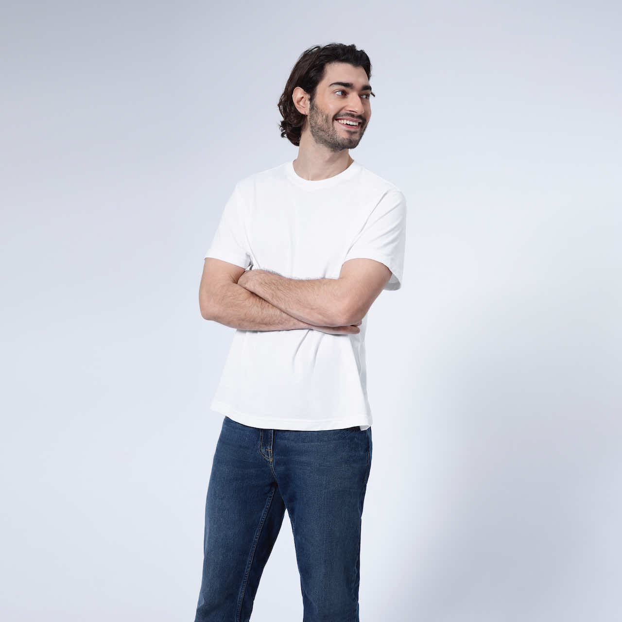 A man looking away from the camera with his arms crossed smiling, modelling a plain white short sleeve organic cotton t shirt.