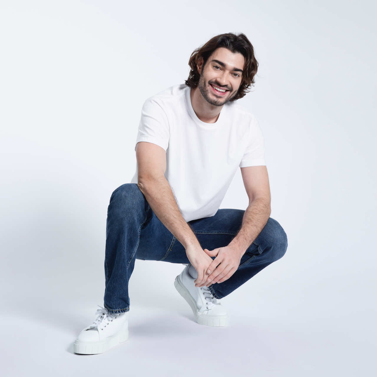 A man crouching down smiling, modelling a plain white short sleeve organic cotton t shirt.