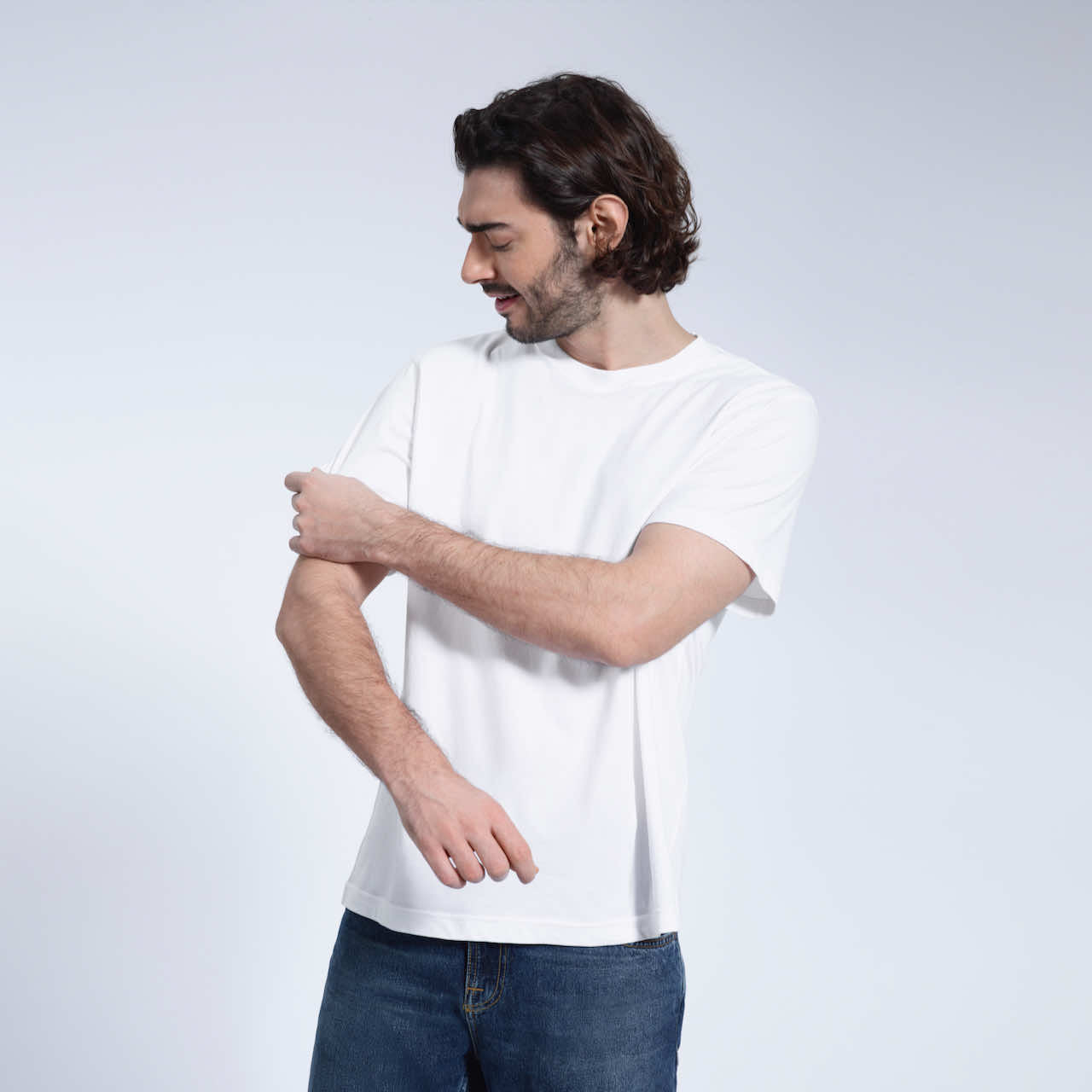 A man looking down and touching his sleeve, modelling a plain white short sleeve organic cotton t shirt.