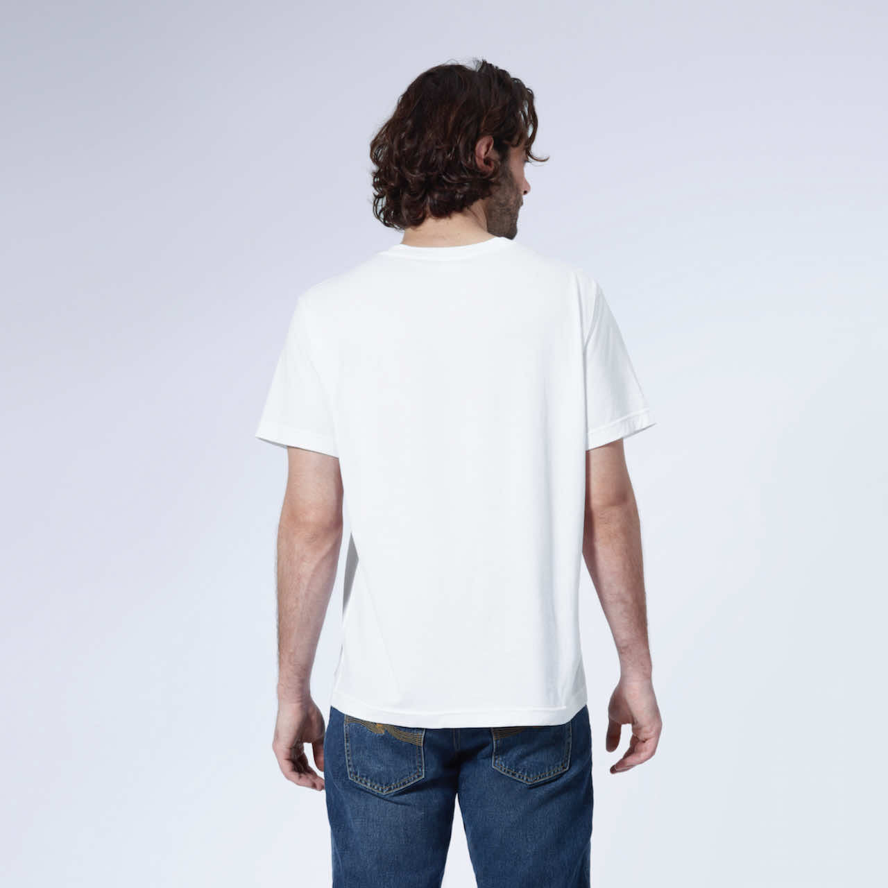 A man facing away from the camera with his arms by his side, modelling a plain white short sleeve organic cotton t shirt.