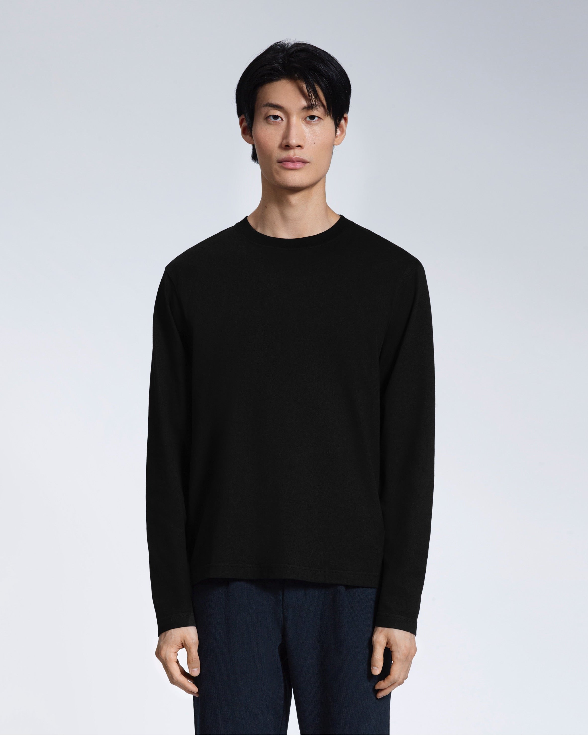 A man standing front on with his arms by his sides, modelling a plain black long sleeve organic cotton t shirt.