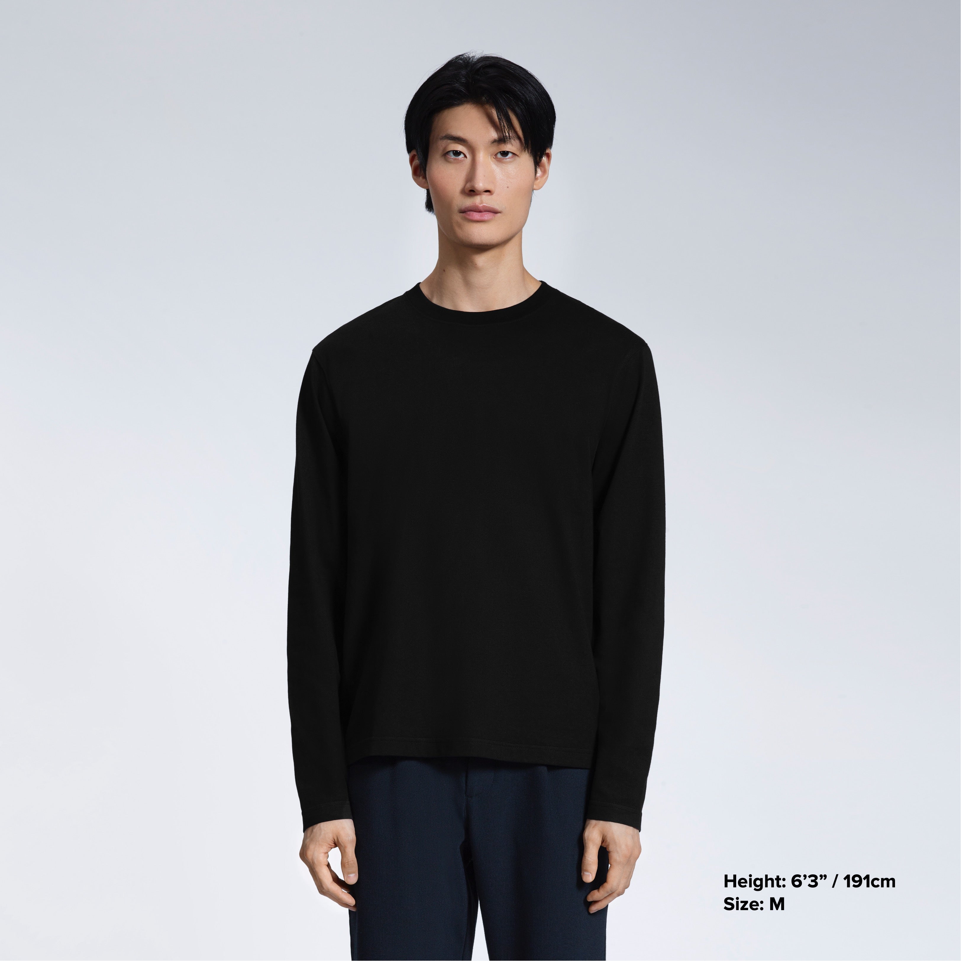 A man standing front on with his arms by his sides, modelling a plain black long sleeve organic cotton t shirt.