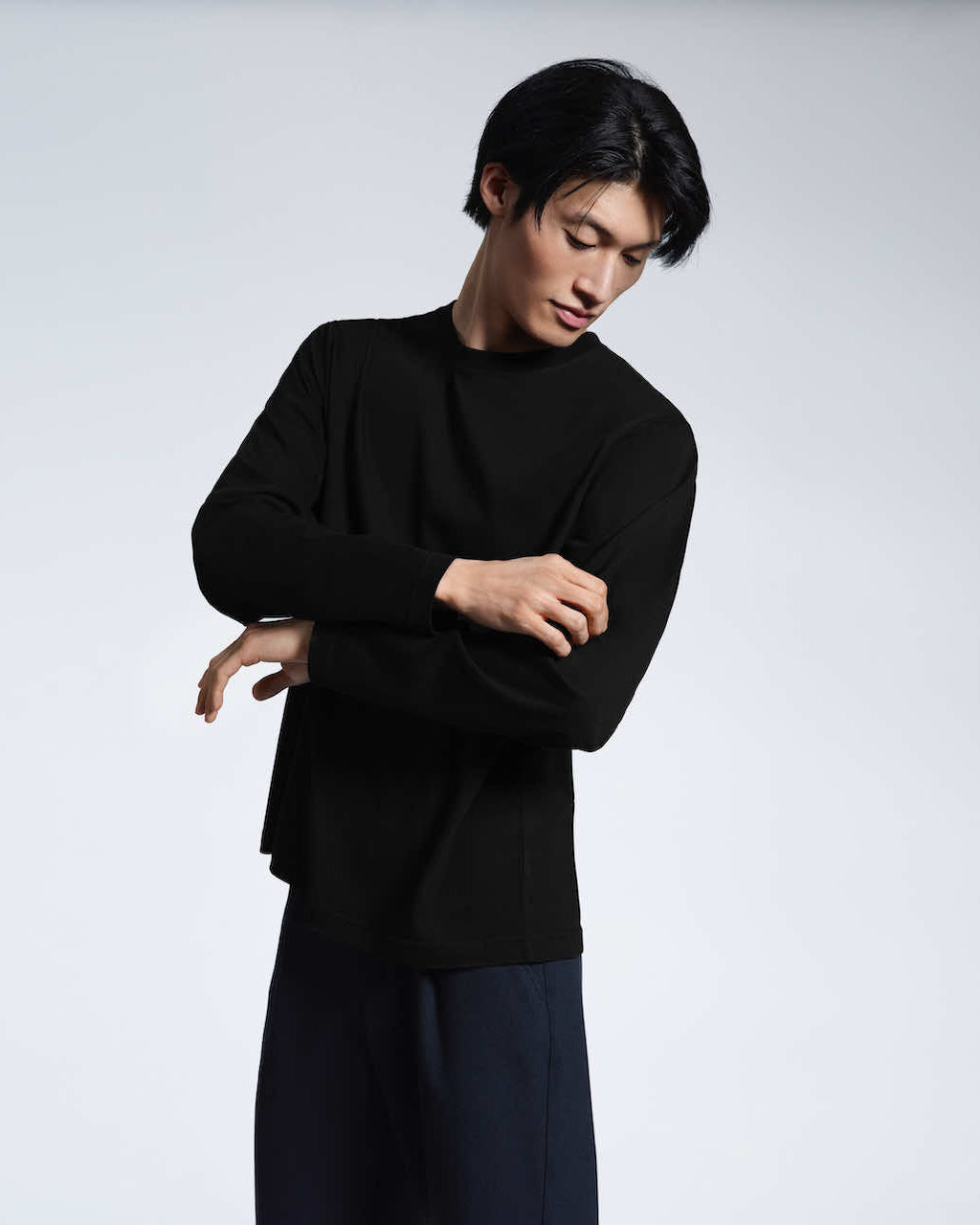 A man looking down and touching his sleeve, modelling a plain black long sleeve organic cotton t shirt.