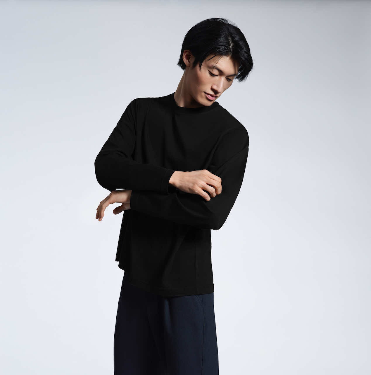 A man looking down and touching his sleeve, modelling a plain black long sleeve organic cotton t shirt.