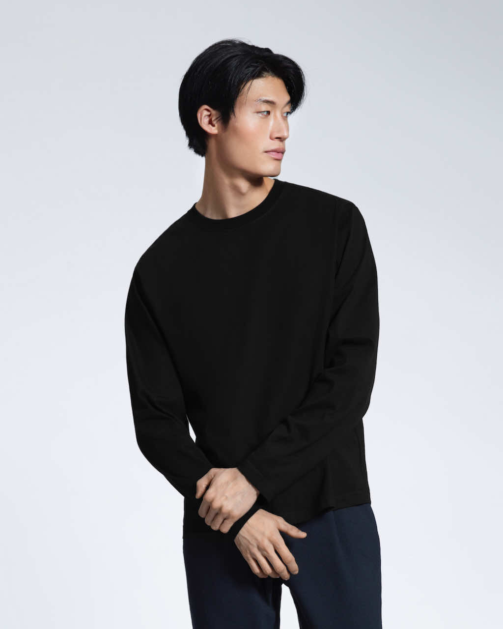 A man with his hands crossed looking away from the camera, modelling a plain black long sleeve organic cotton t shirt.