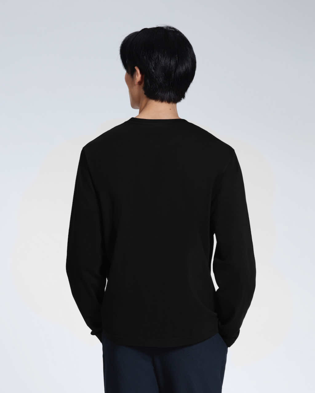 A man facing away from the camera with his hands in his pockets, modelling a plain black long sleeve organic cotton t shirt.