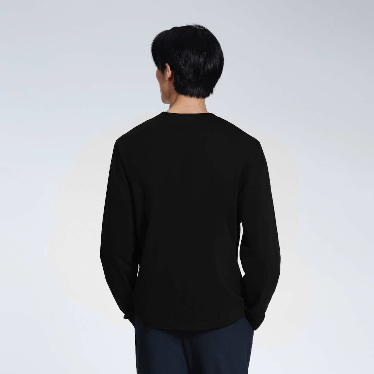 A man facing away from the camera with his hands in his pockets, modelling a plain black long sleeve organic cotton t shirt.