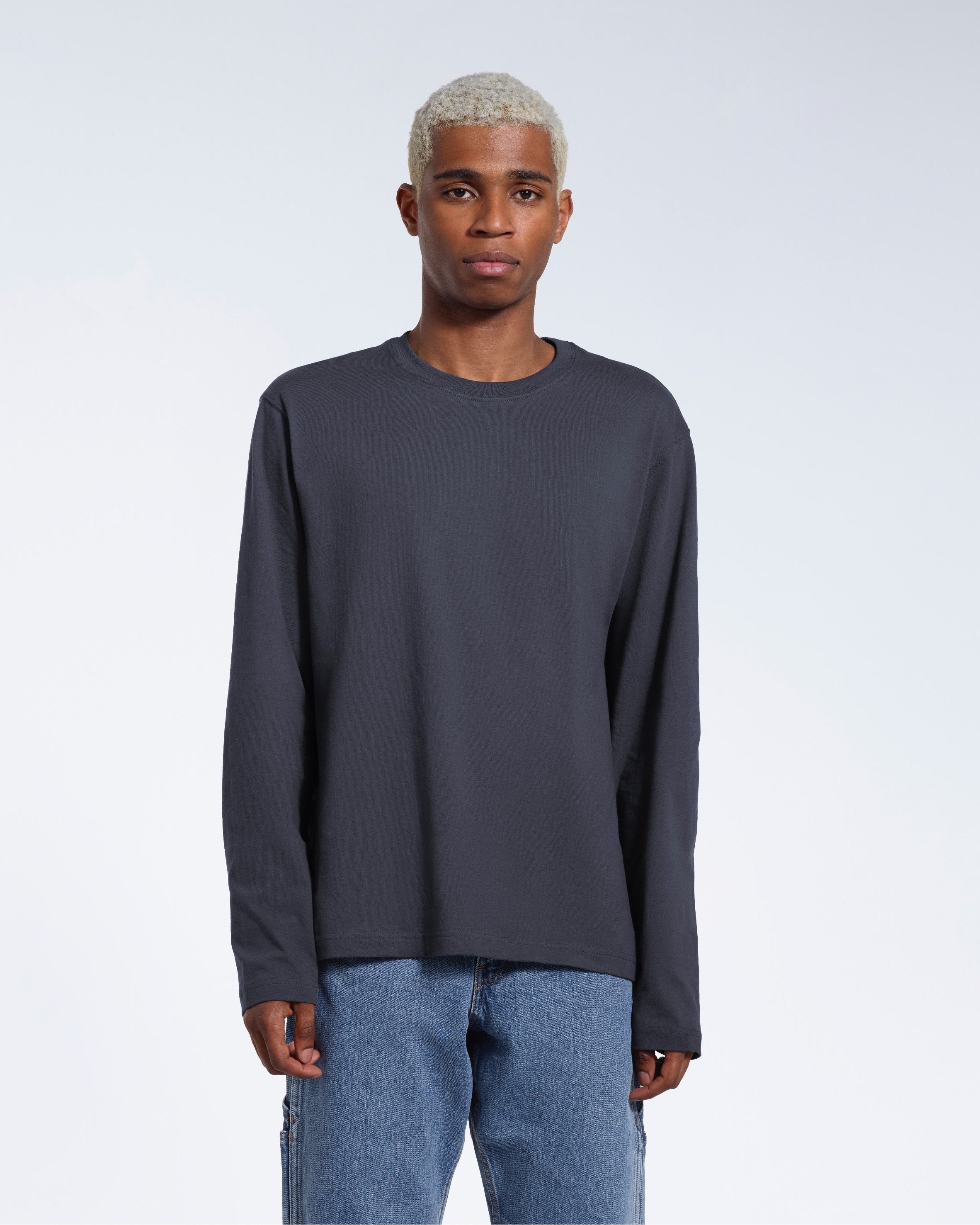 A man standing front on with his arms by his sides, modelling a plain dark grey long sleeve organic cotton t shirt.