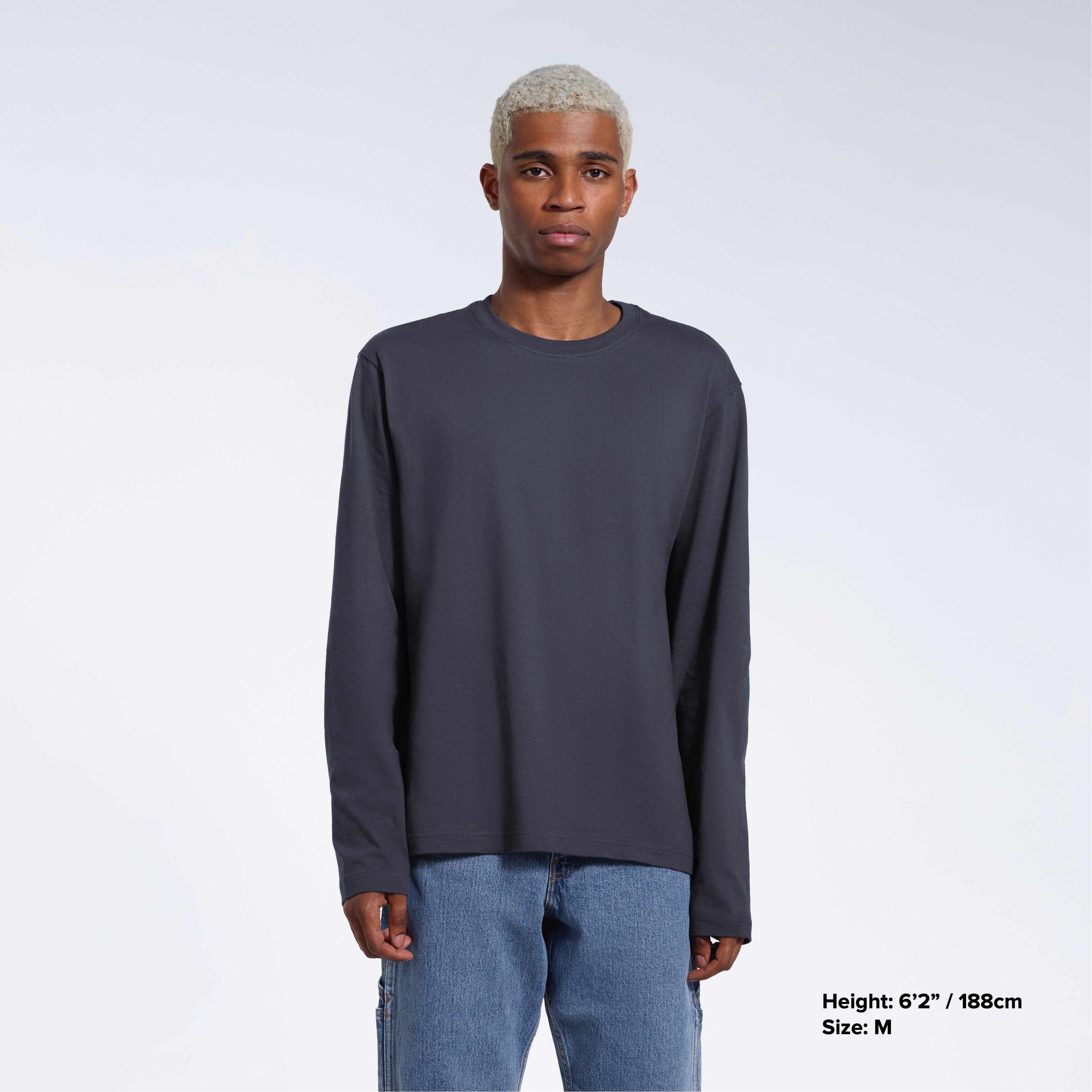 A man standing front on with his arms by his sides, modelling a plain dark grey long sleeve organic cotton t shirt.