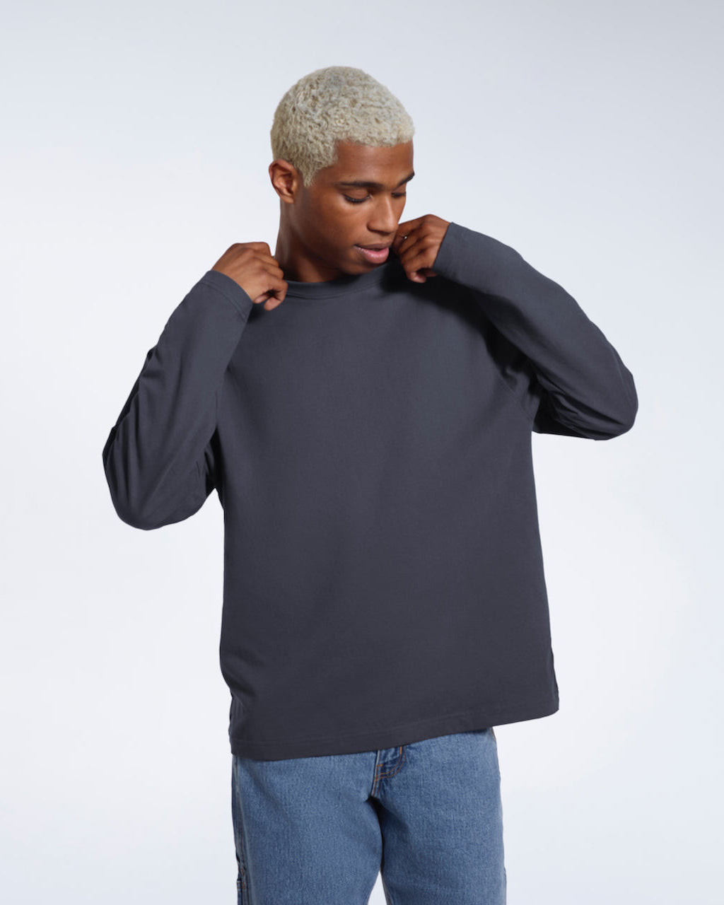 A man looking down and touching his collar, modelling a plain dark grey long sleeve organic cotton t shirt.