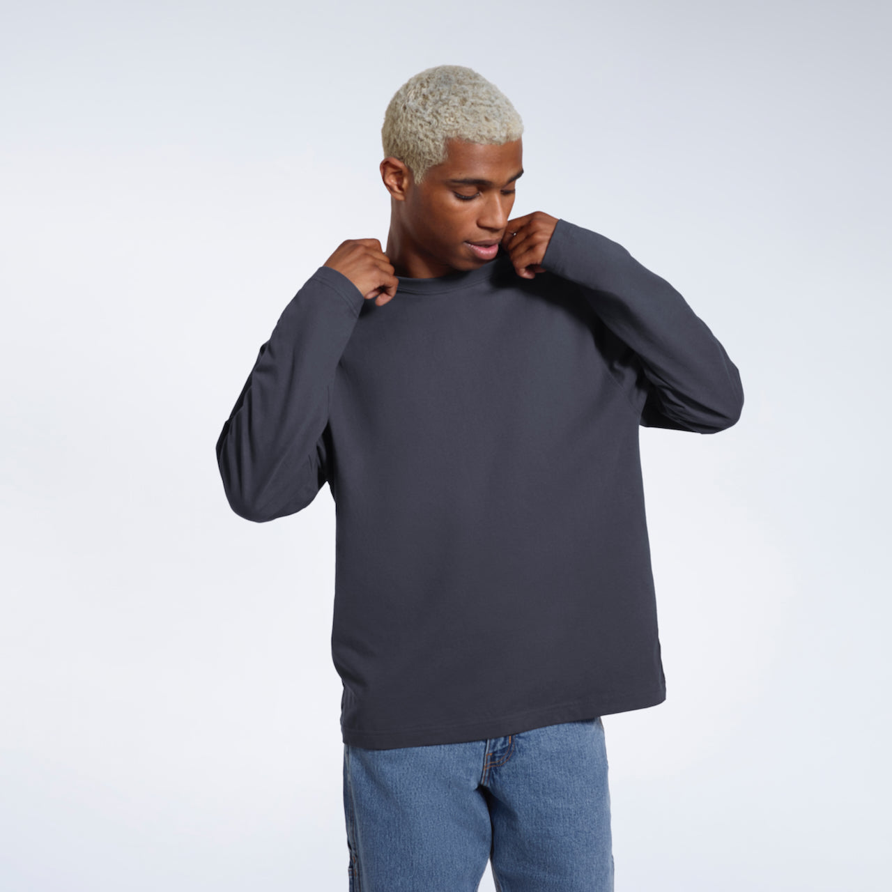 A man looking down and touching his collar, modelling a plain dark grey long sleeve organic cotton t shirt.