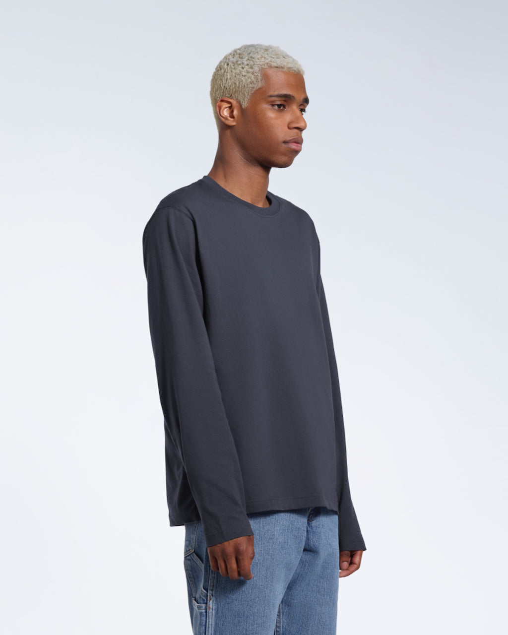 A man looking away from the camera with his arms by his sides, modelling a plain dark grey long sleeve organic cotton t shirt.