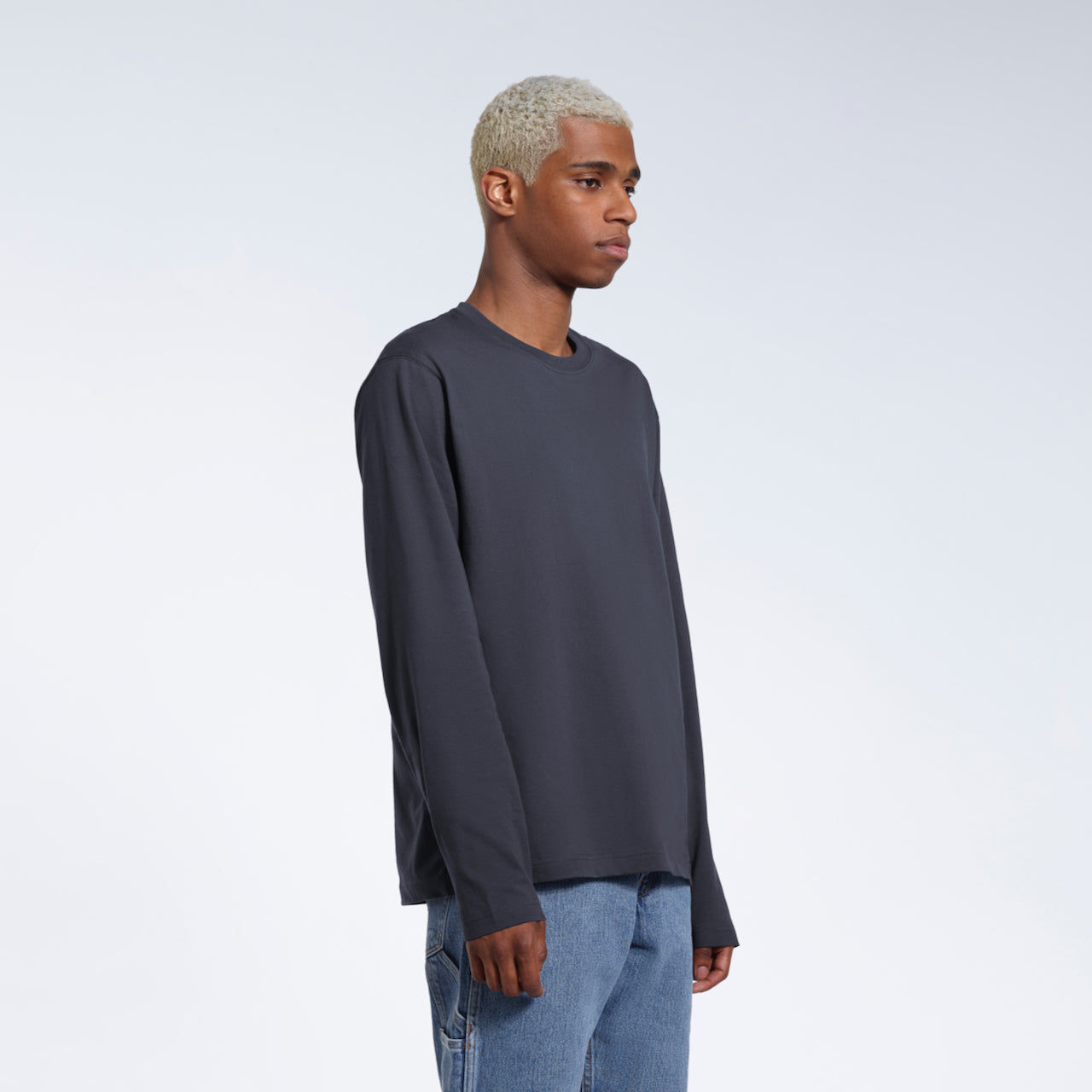 A man looking away from the camera with his arms by his sides, modelling a plain dark grey long sleeve organic cotton t shirt.