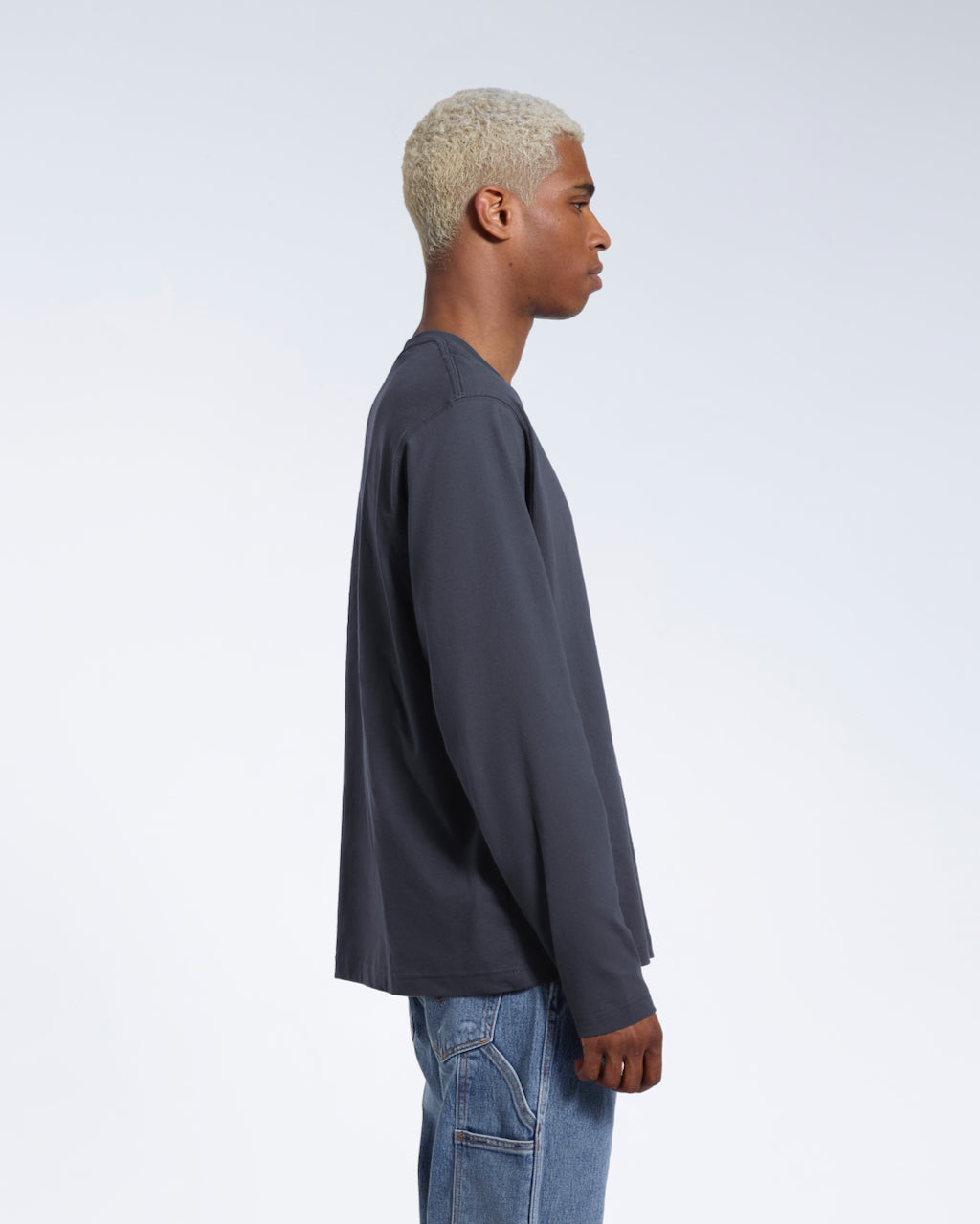A man facing side on with his arms by his sides, modelling a plain dark grey long sleeve organic cotton t shirt.