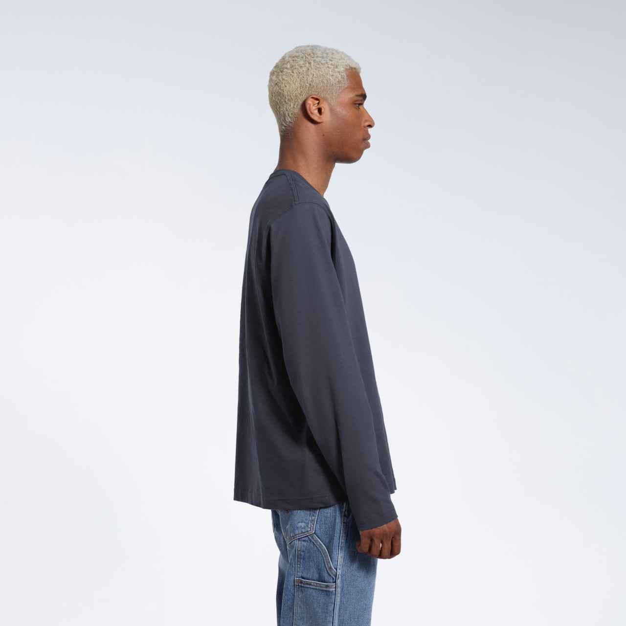 A man facing side on with his arms by his sides, modelling a plain dark grey long sleeve organic cotton t shirt.