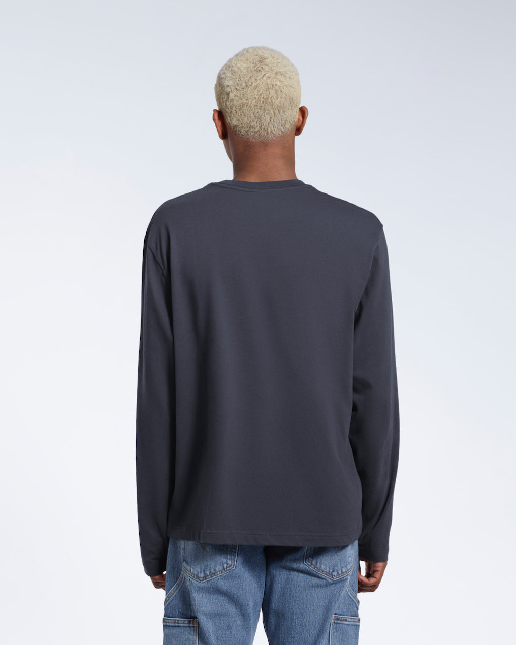 A man facing away from the camera with his arms by his sides, modelling a plain dark grey long sleeve organic cotton t shirt.