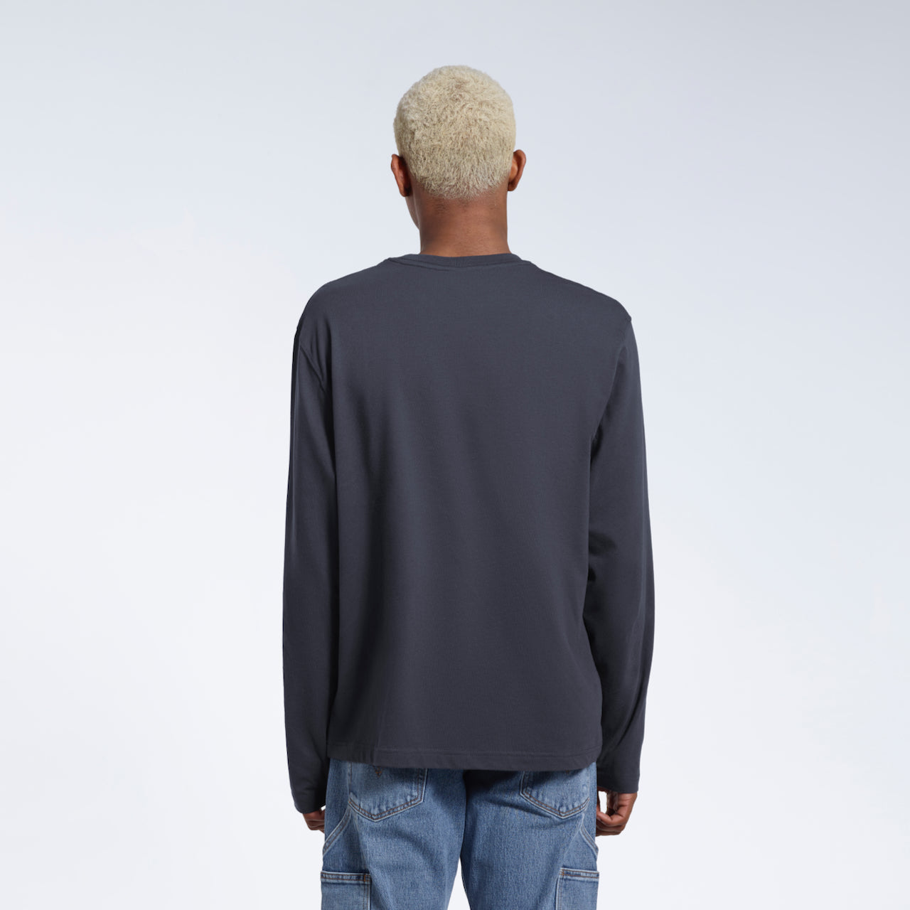 A man facing away from the camera with his arms by his sides, modelling a plain dark grey long sleeve organic cotton t shirt.