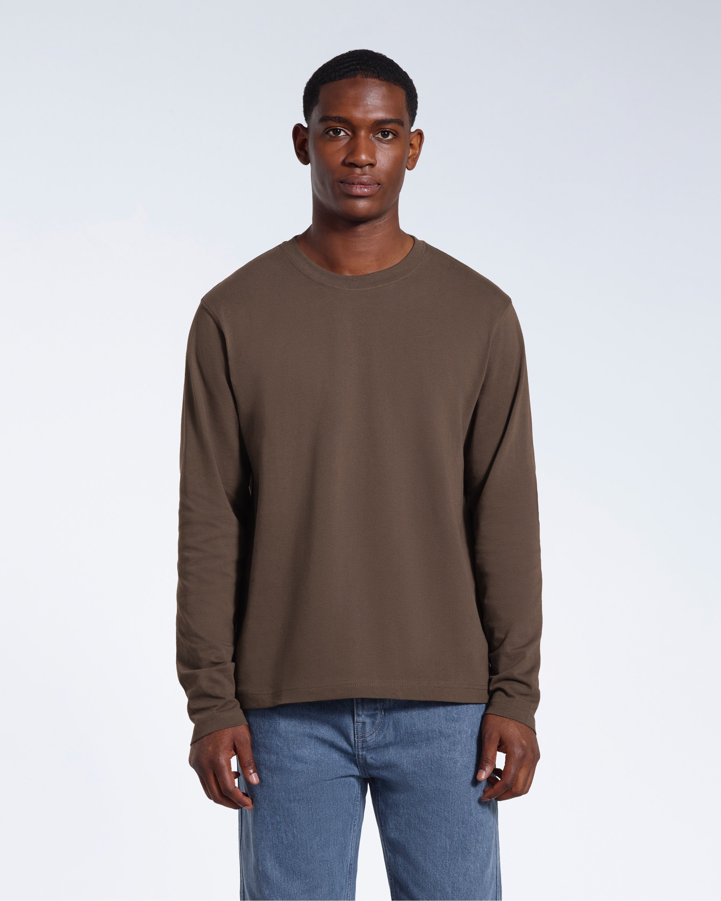 A man standing front on with his arms by his sides, modelling a plain dark khaki long sleeve organic cotton t shirt.