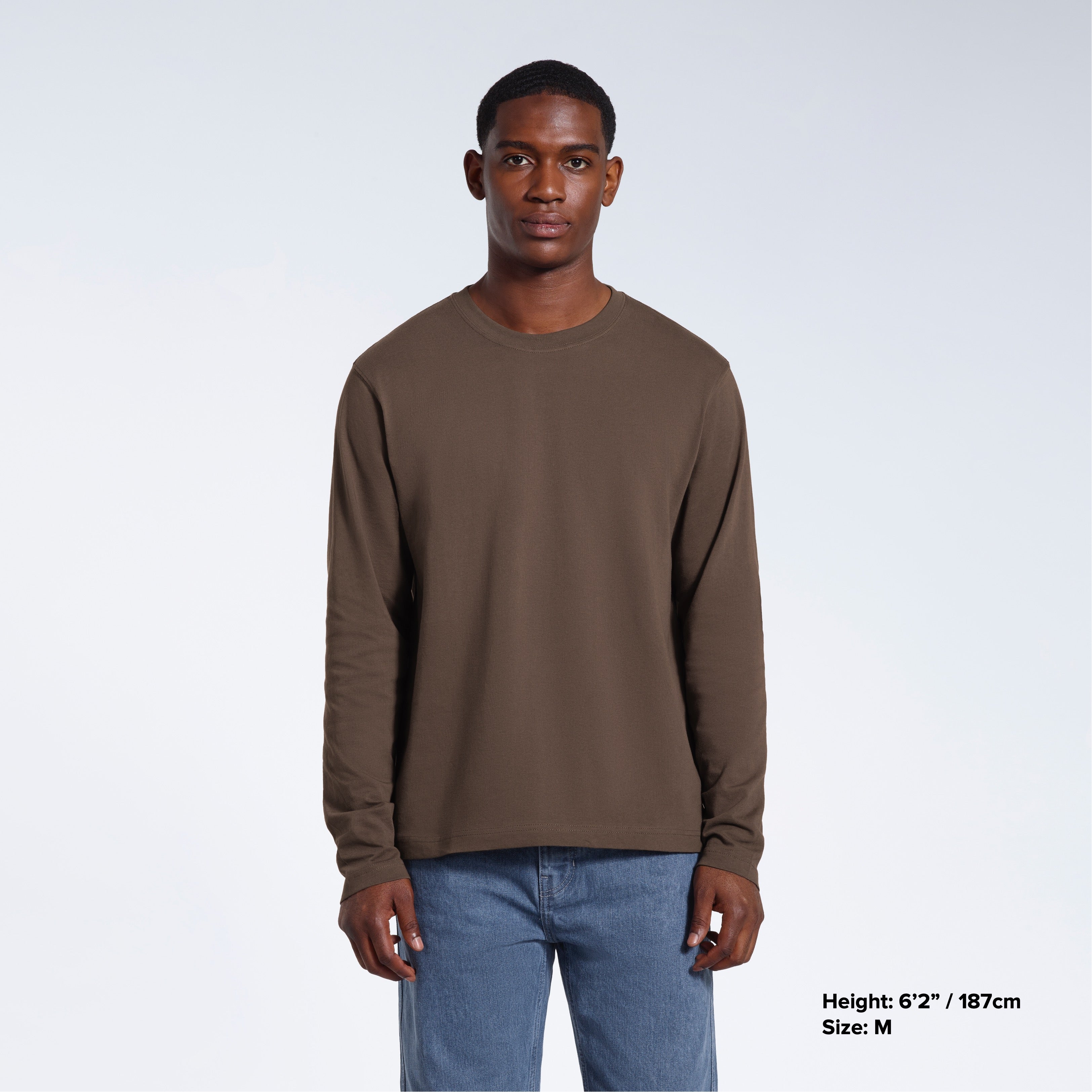 A man standing front on with his arms by his sides, modelling a plain dark khaki long sleeve organic cotton t shirt.