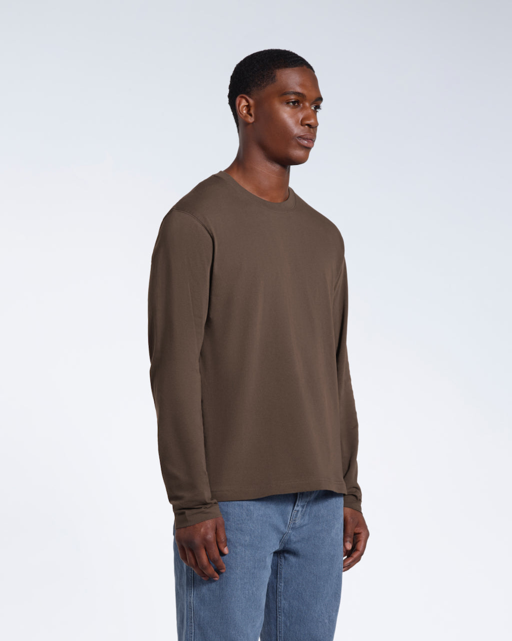 A man looking away from the camera with his arms by his sides, modelling a plain dark khaki long sleeve organic cotton t shirt.