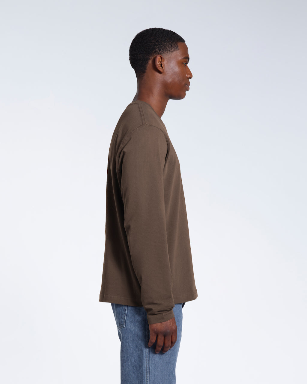 A man facing side on with his arms by his sides, modelling a plain dark khaki long sleeve organic cotton t shirt.