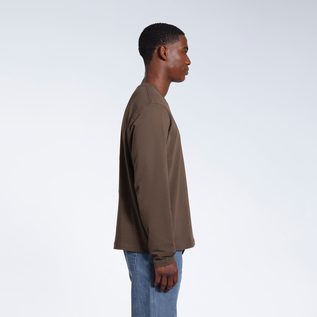A man facing side on with his arms by his sides, modelling a plain dark khaki long sleeve organic cotton t shirt.
