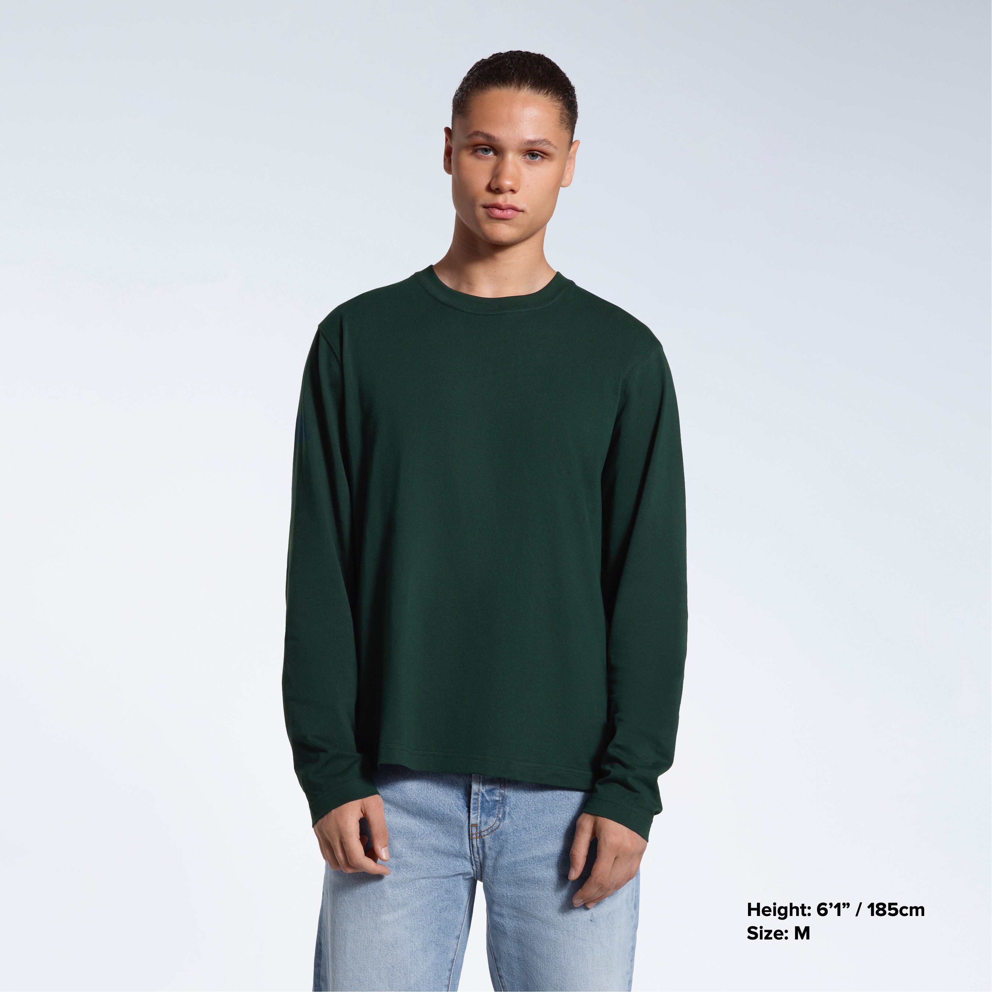 A man standing front on with his arms by his sides, modelling a plain green long sleeve organic cotton t shirt.
