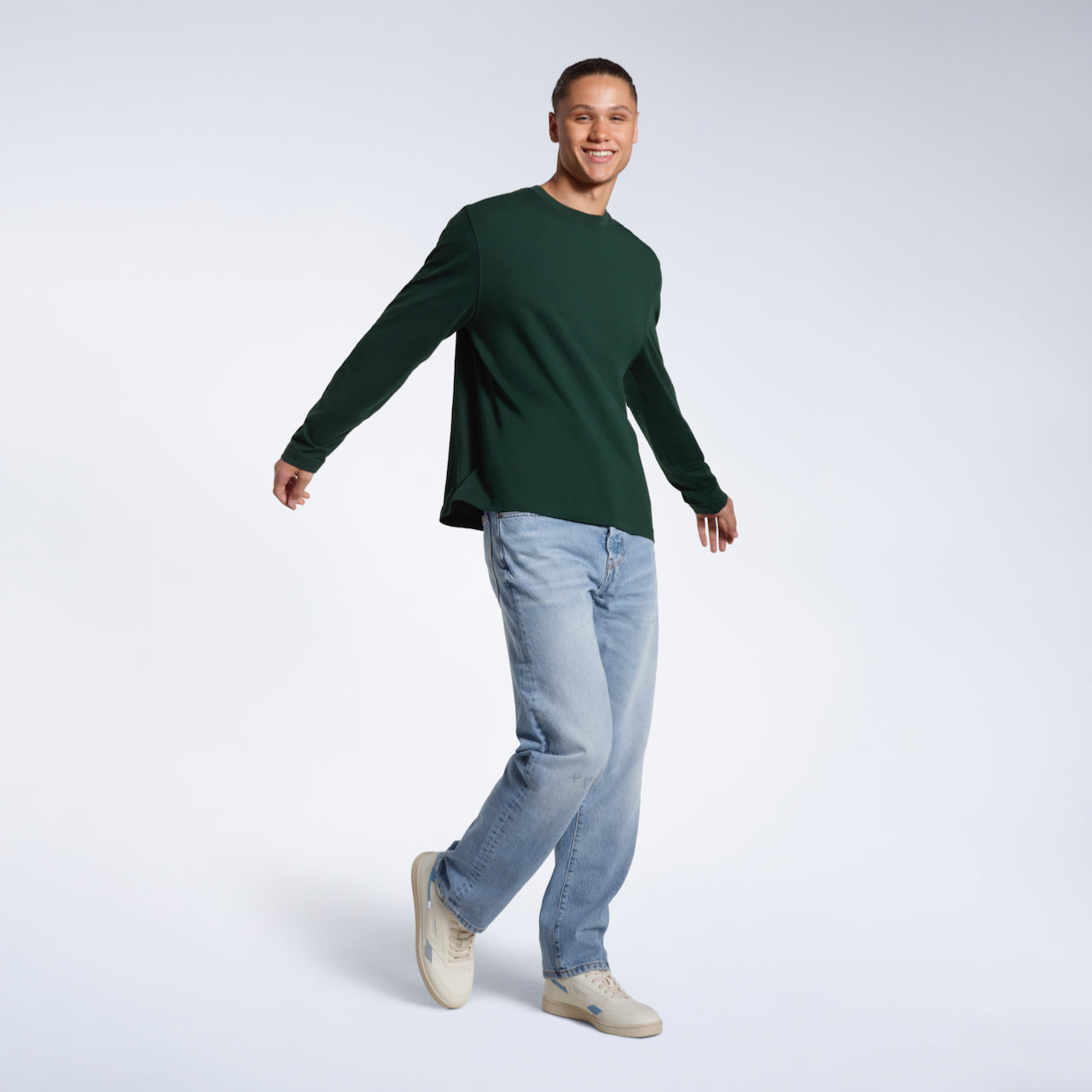 A man walking and smiling, modelling a plain green long sleeve organic cotton t shirt.