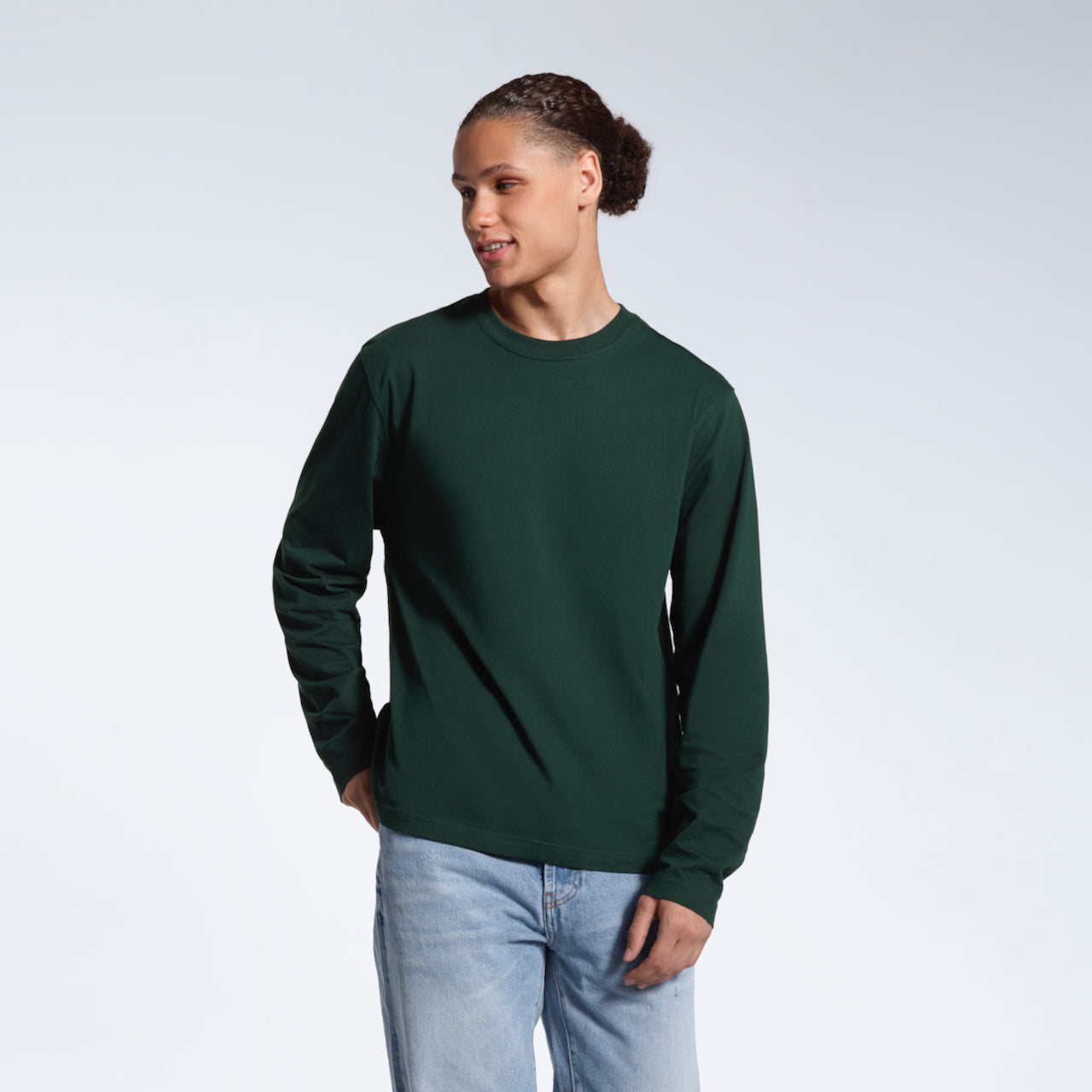 A man looking away from the camera with his hand in his back pocket, modelling a plain green long sleeve organic cotton t shirt.