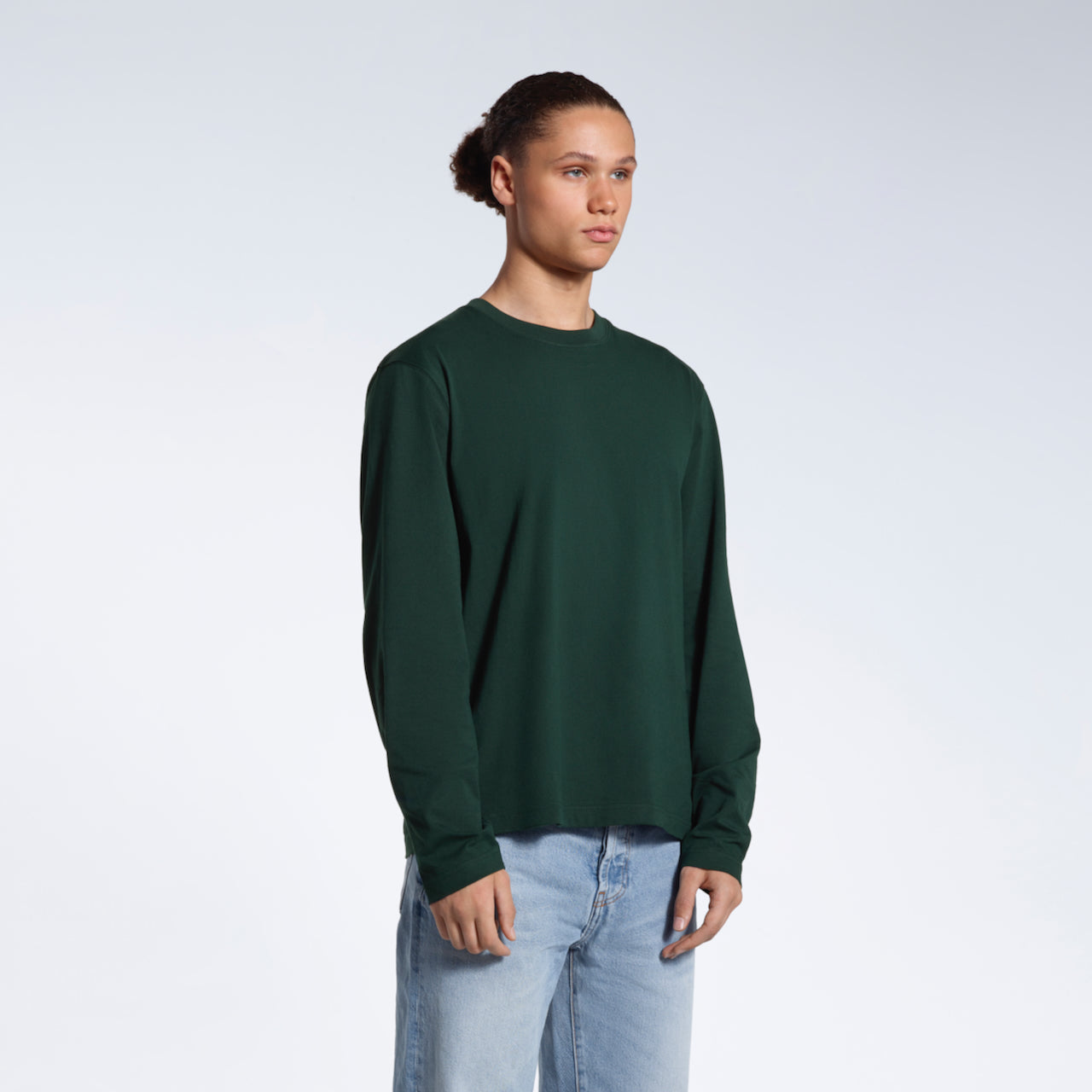 A man looking away from the camera with his arms by his sides, modelling a plain green long sleeve organic cotton t shirt.