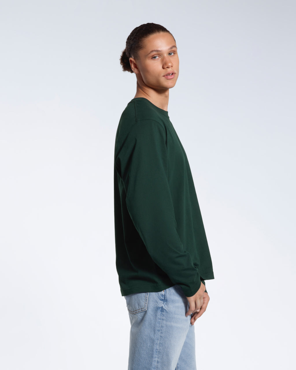 A man facing side on looking back at the camera, modelling a plain green long sleeve organic cotton t shirt.