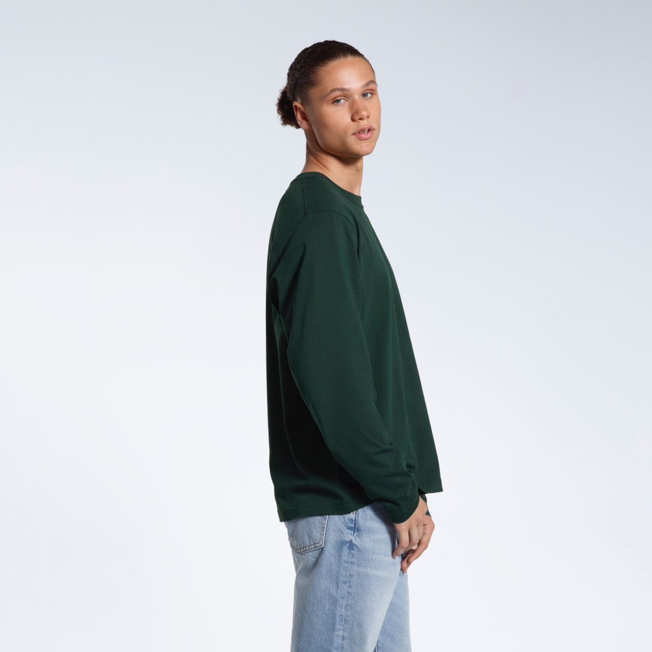 A man facing side on looking back at the camera, modelling a plain green long sleeve organic cotton t shirt.