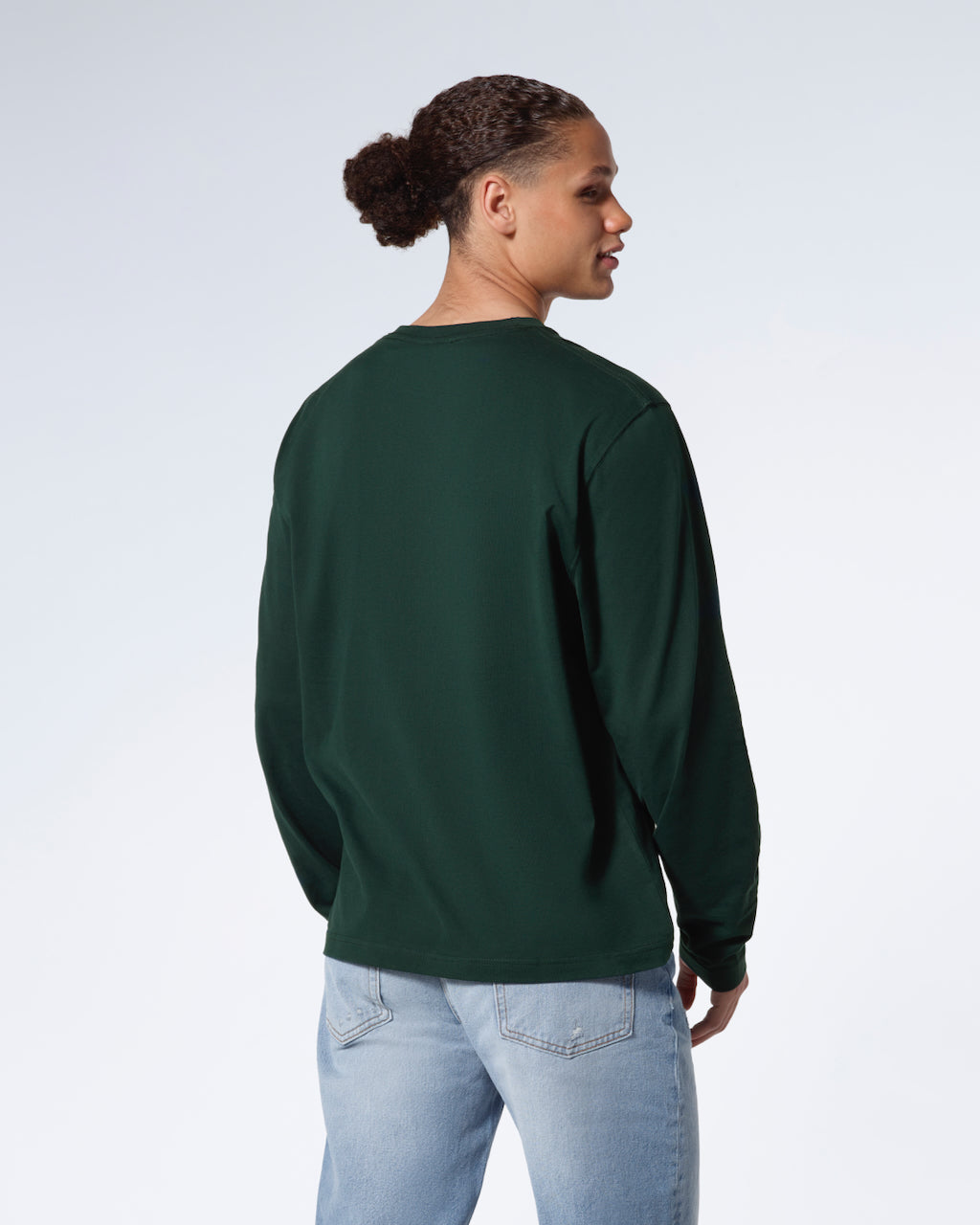 A man facing away from the camera with his arms by his sides, modelling a plain green long sleeve organic cotton t shirt.