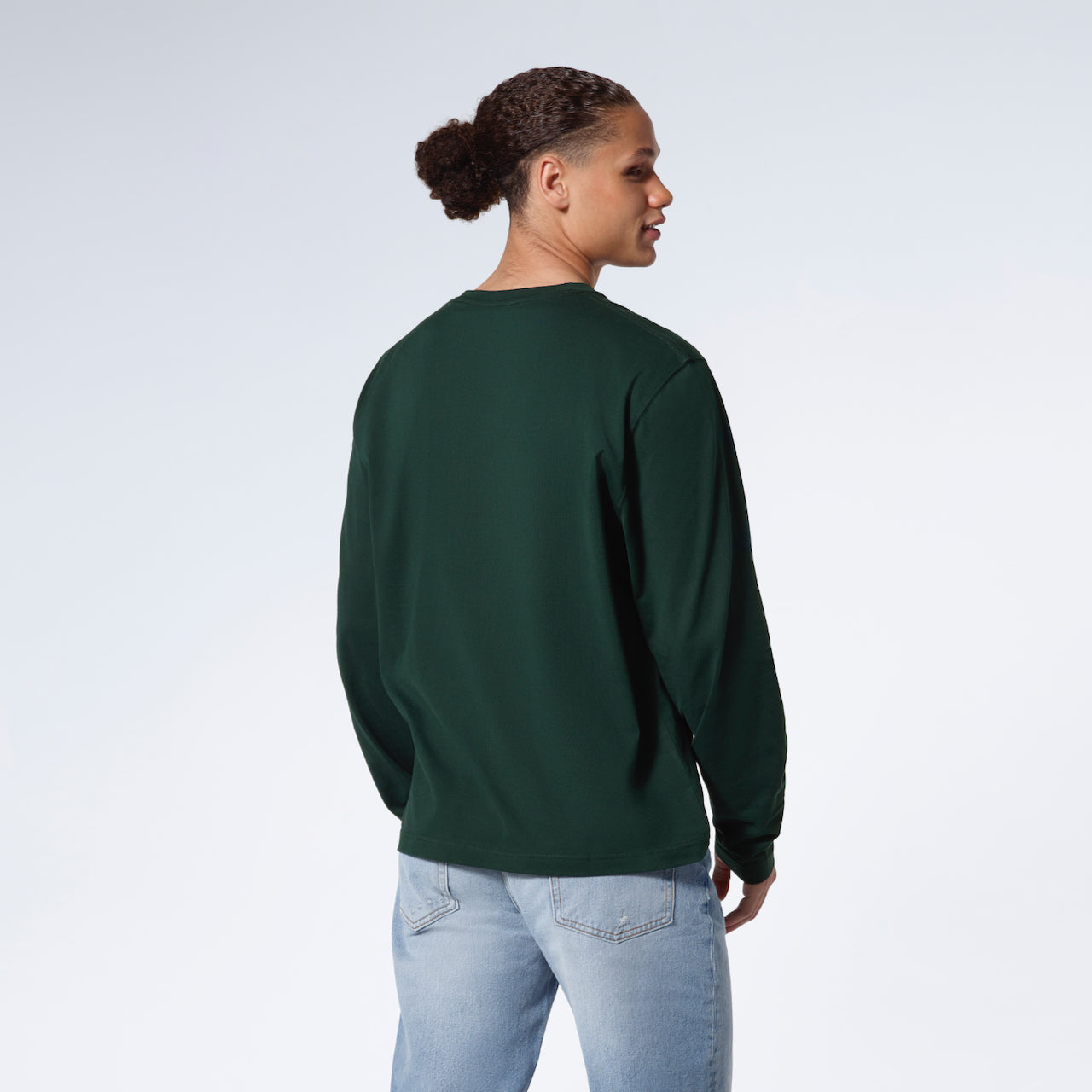 A man facing away from the camera with his arms by his sides, modelling a plain green long sleeve organic cotton t shirt.