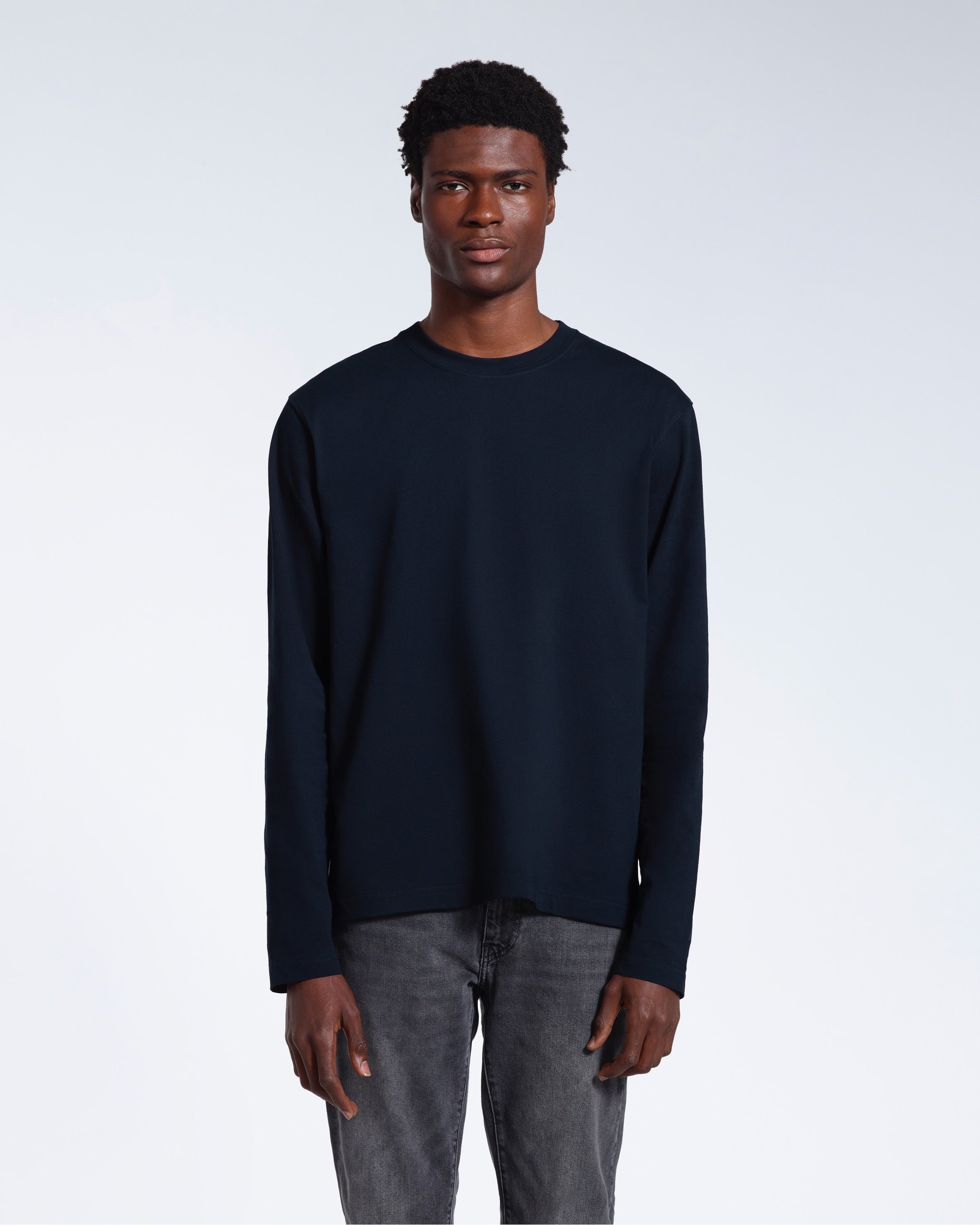 A man standing front on with his arms by his sides, modelling a plain navy long sleeve organic cotton t shirt.