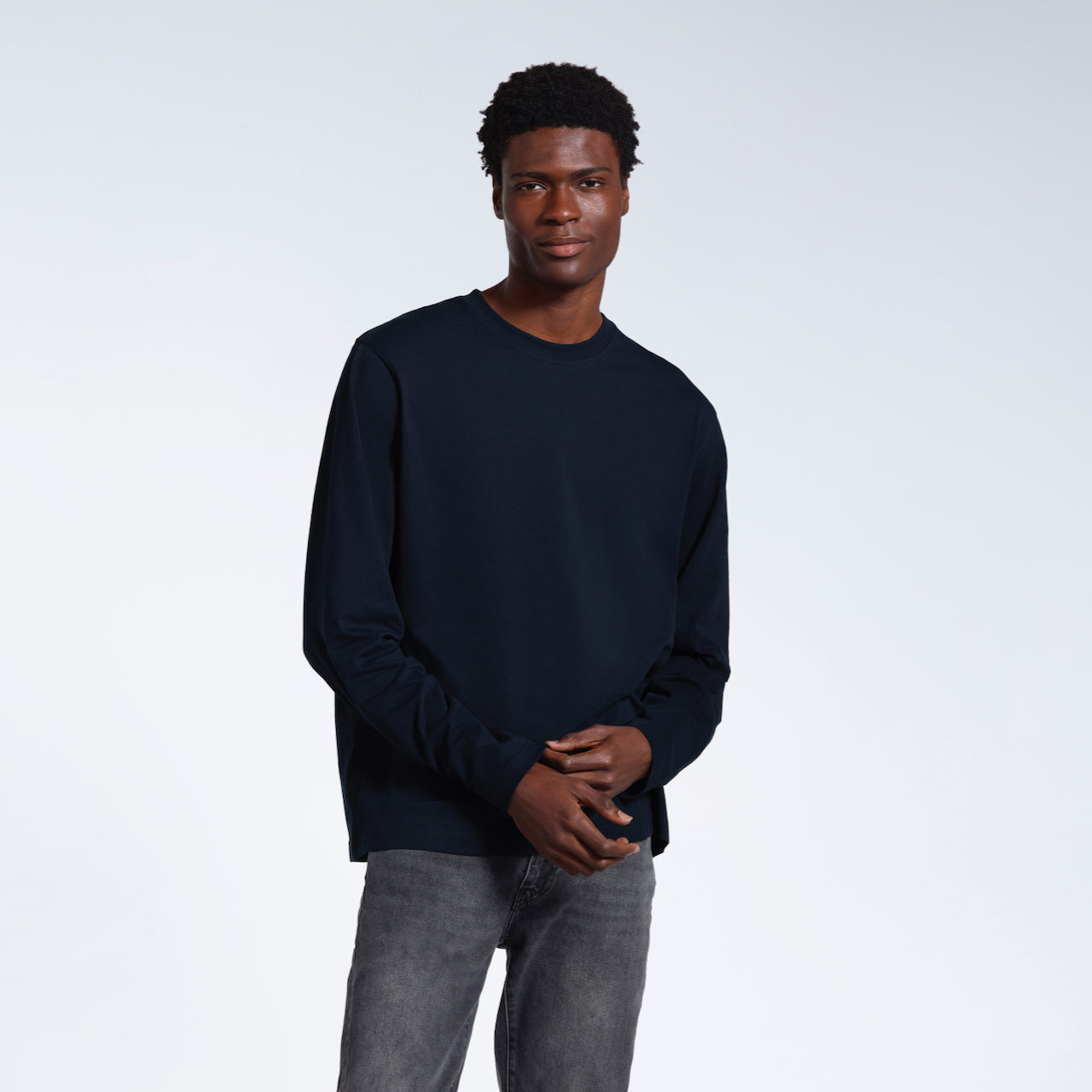 A man looking into the camera, touching the sleeve of his plain navy long sleeve organic cotton t shirt.