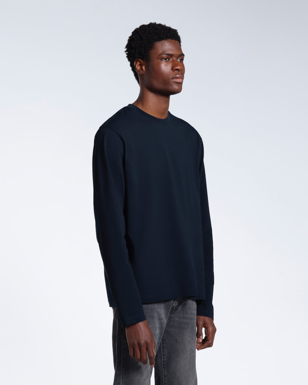 A man looking away from the camera with his arms by his sides, modelling a plain navy long sleeve organic cotton t shirt.