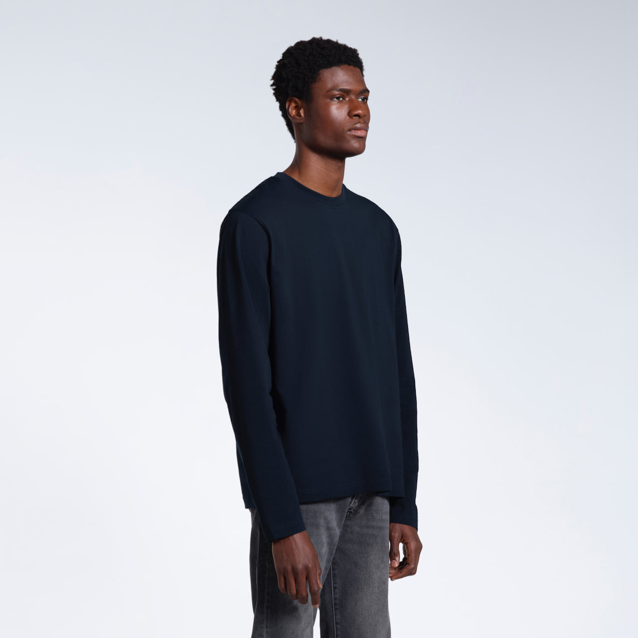 A man looking away from the camera with his arms by his sides, modelling a plain navy long sleeve organic cotton t shirt.