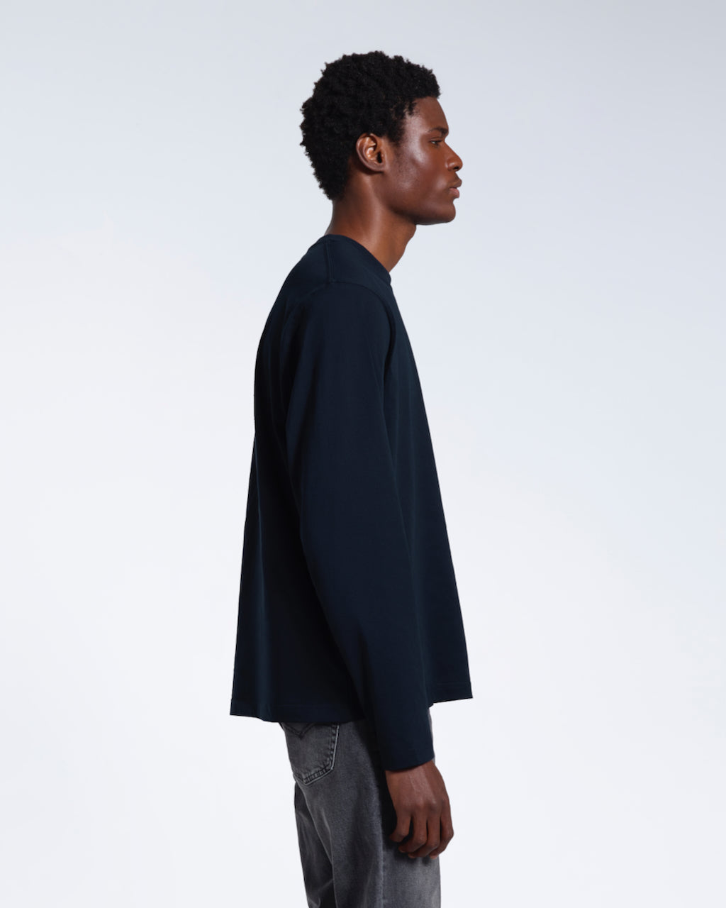 A man facing side on with his arms by his sides, modelling a plain navy long sleeve organic cotton t shirt.